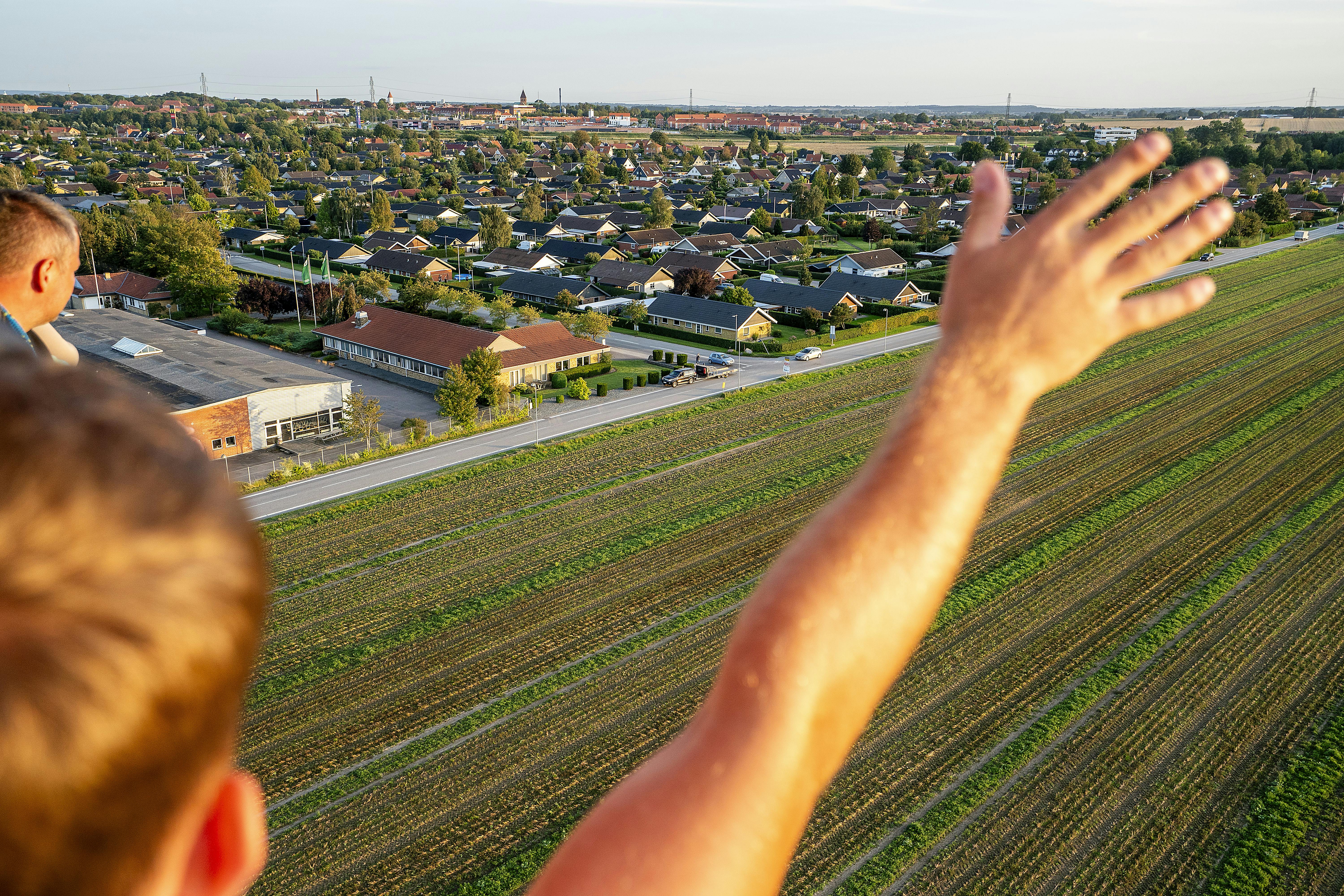 En passager på luftballonen fra DreamBalloon vinker til de mennesker, der er steget ud af bilen for at være tilskuere.