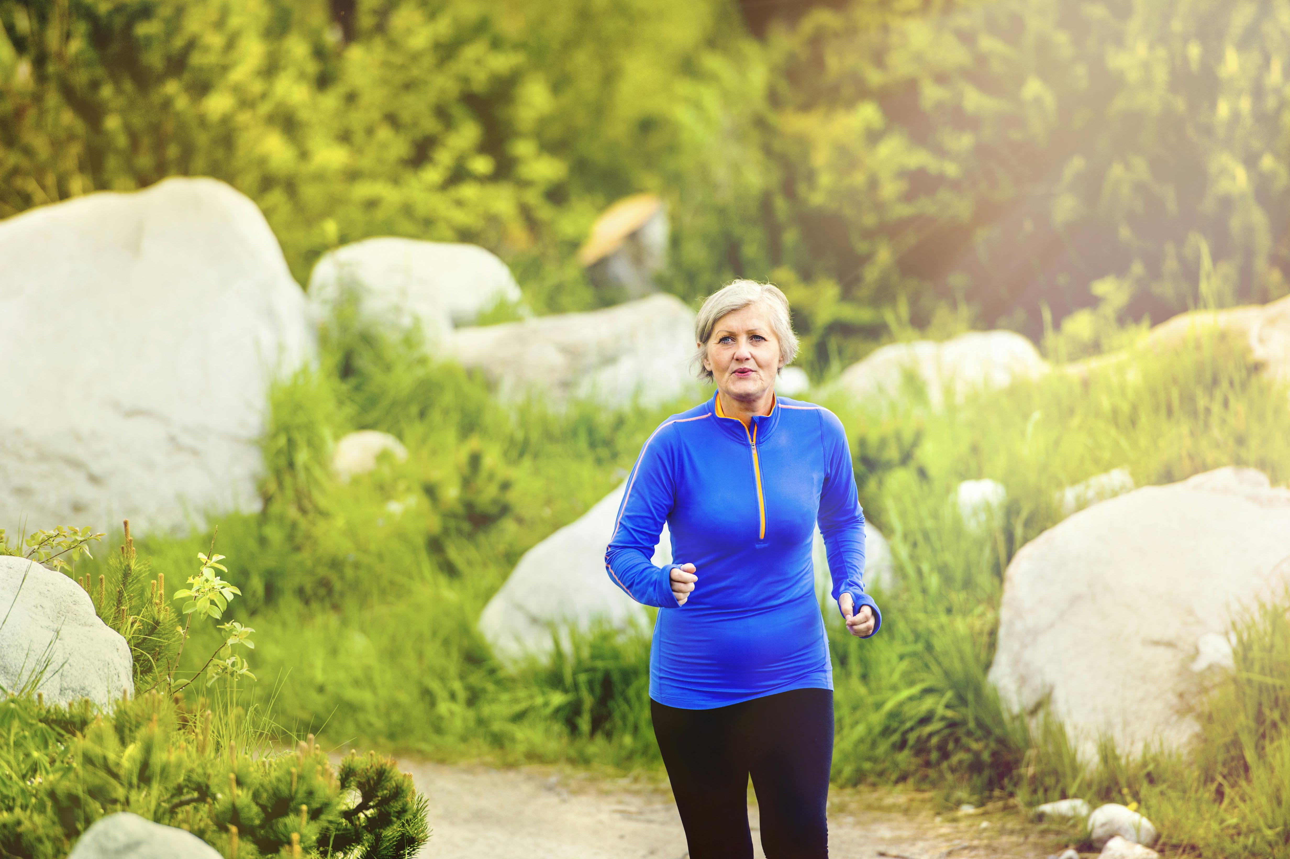 Senior woman jogging in beautiful nature, rocks in background