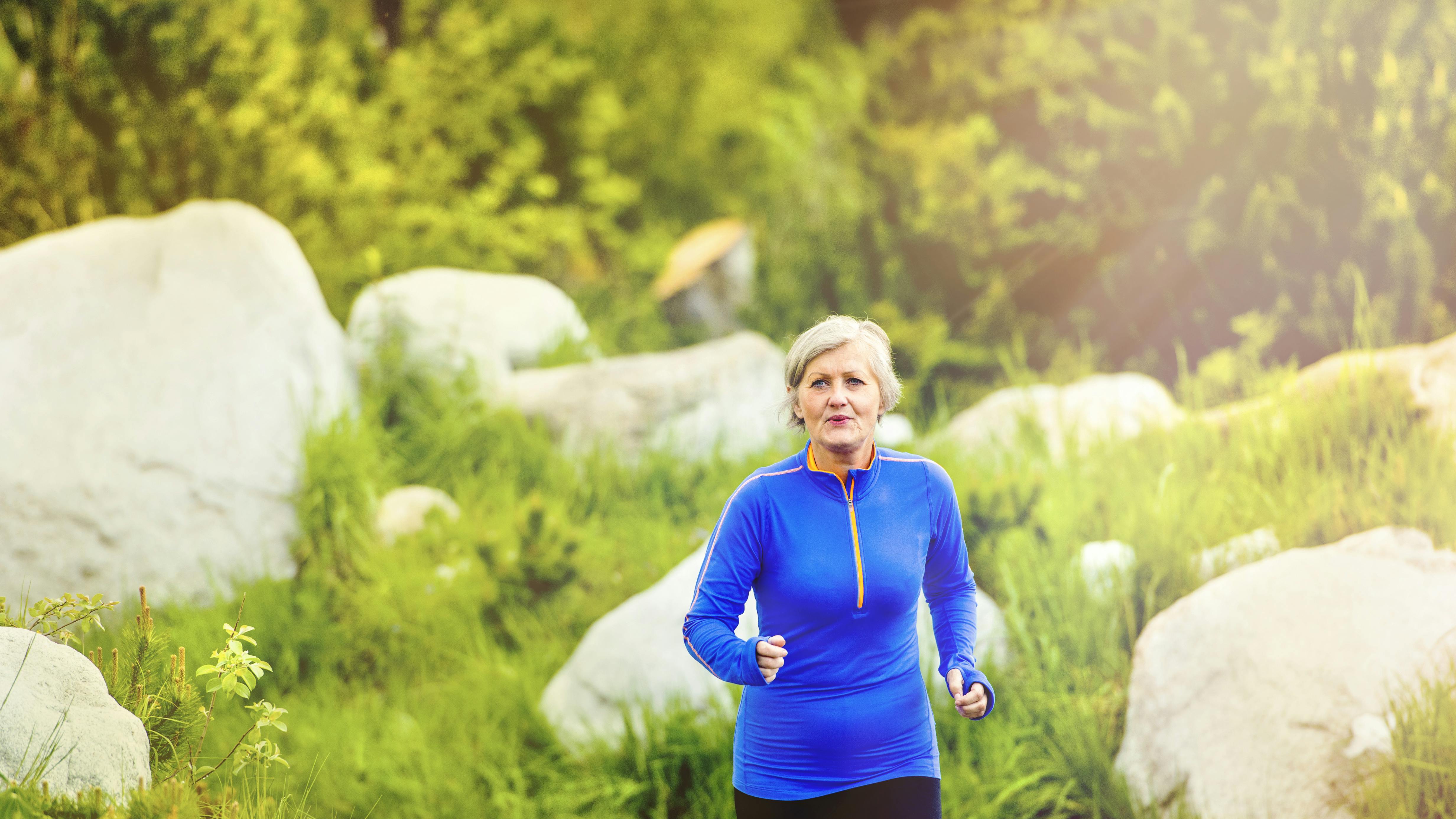 Senior woman jogging in beautiful nature, rocks in background