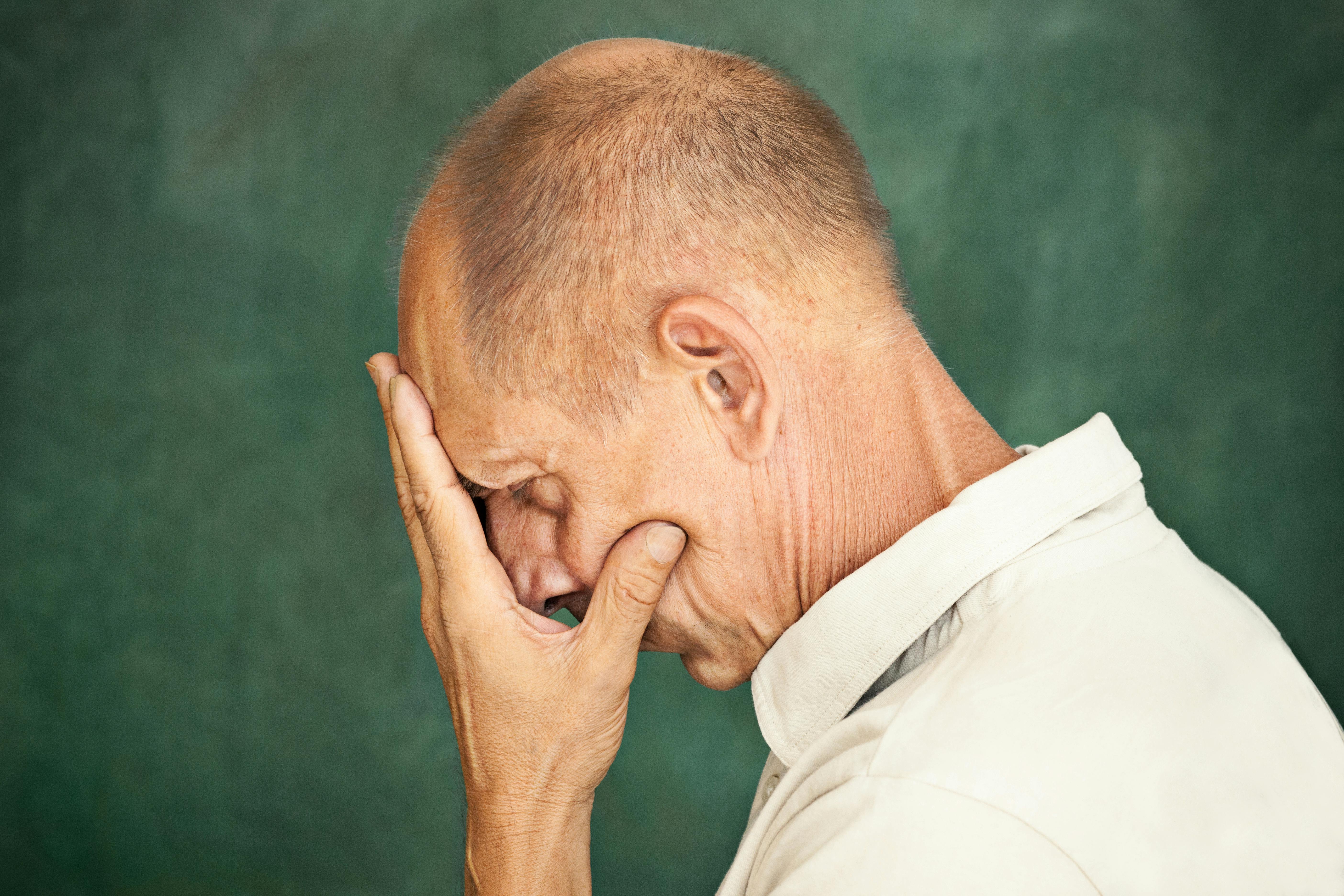 Worried mature man touching his head and thinking on studio background.