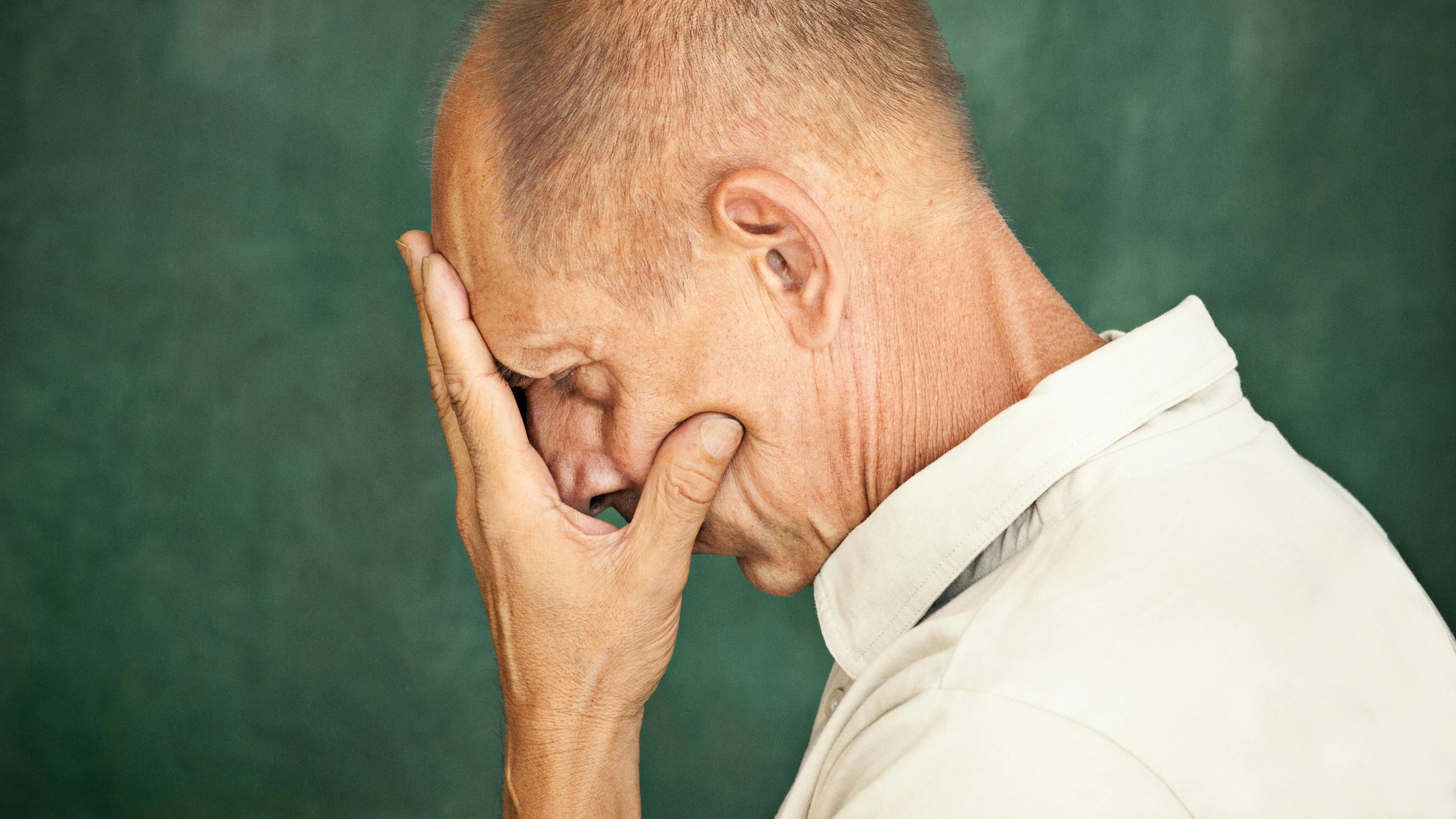 Worried mature man touching his head and thinking on studio background.