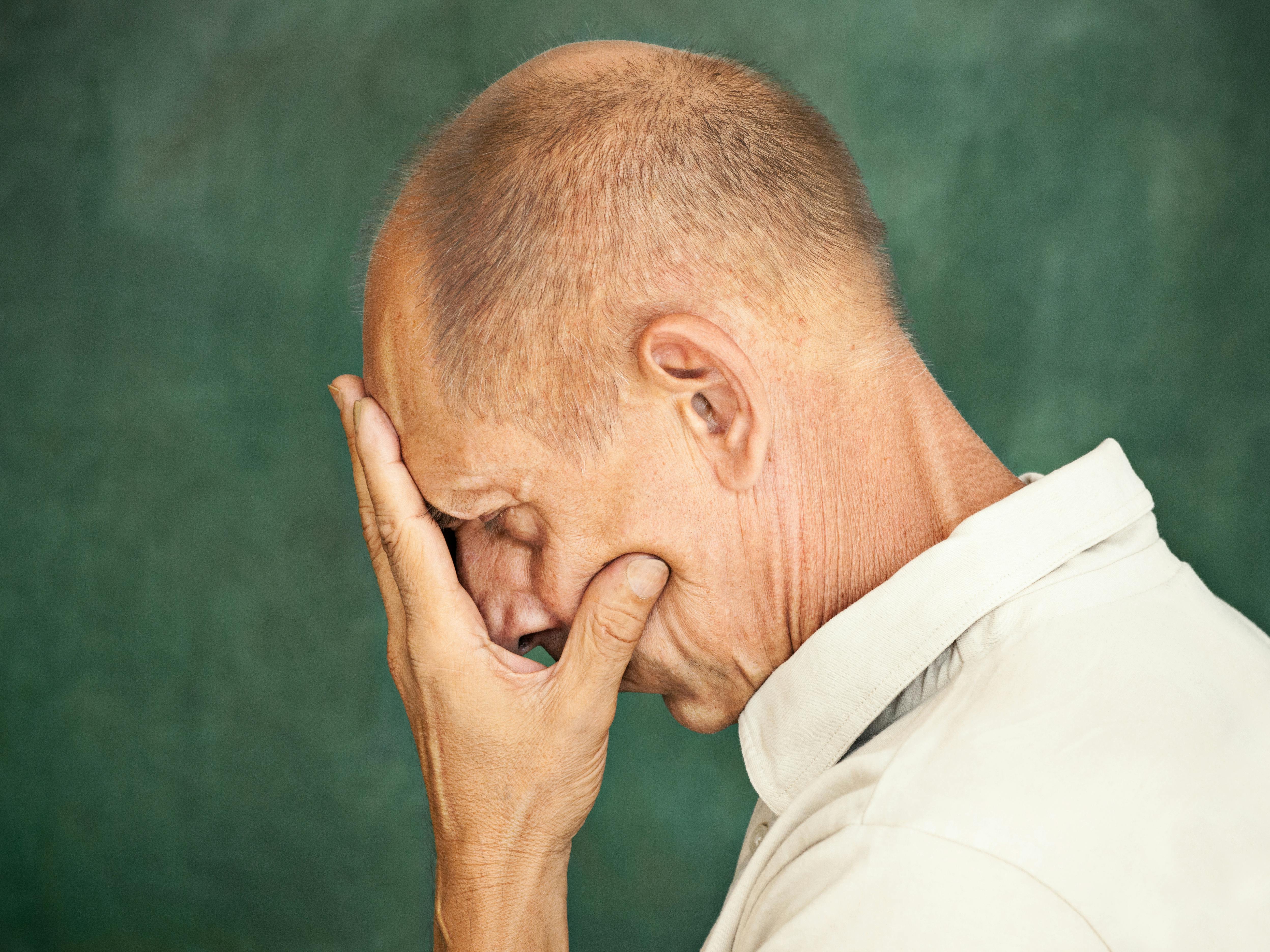 Worried mature man touching his head and thinking on studio background.