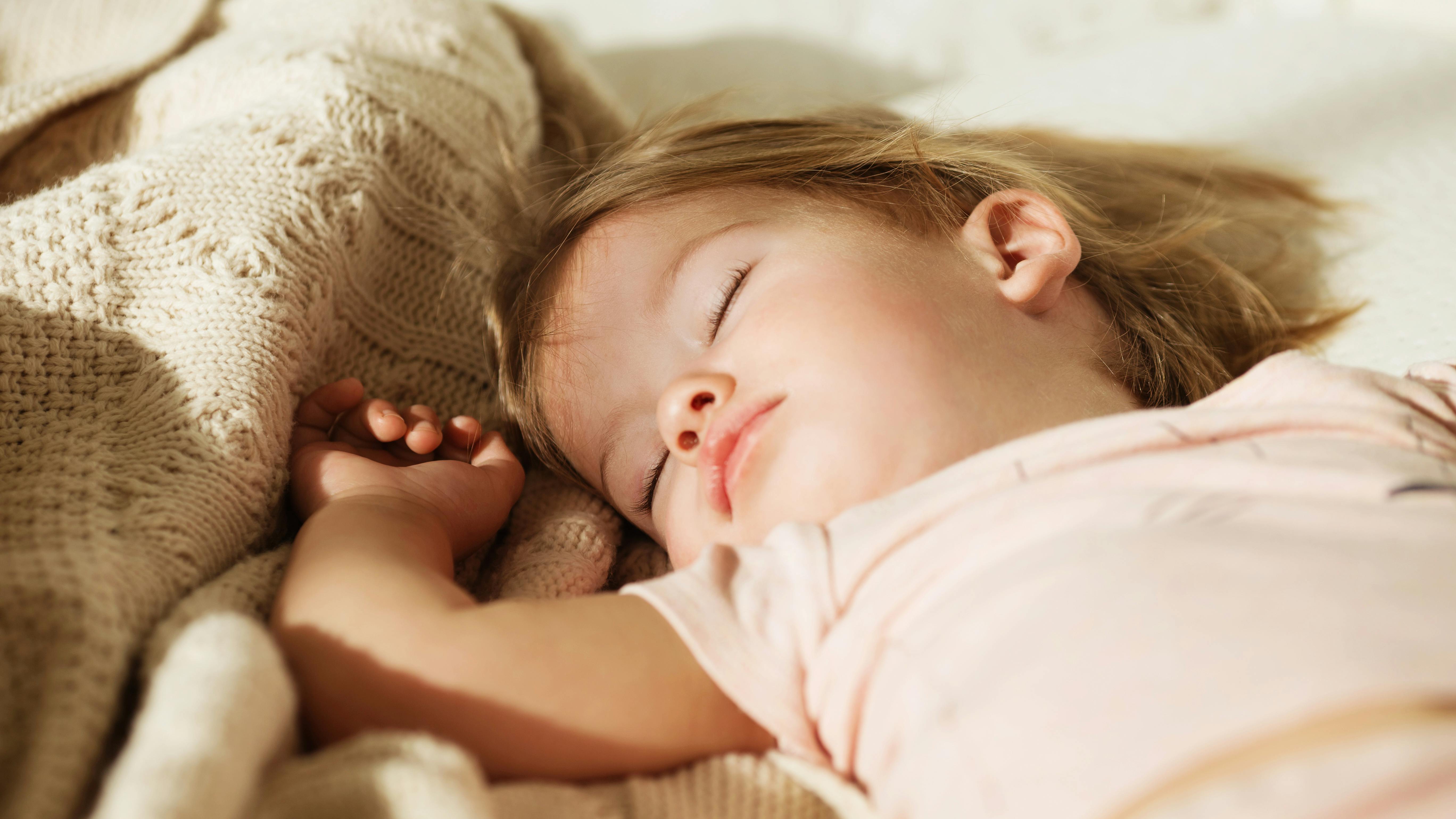 Sleeping little girl. Carefree sleep little baby with a soft toy on the bed. Close-up portrait of a beautiful sleeping child on knitted blanket. Sweet dreams