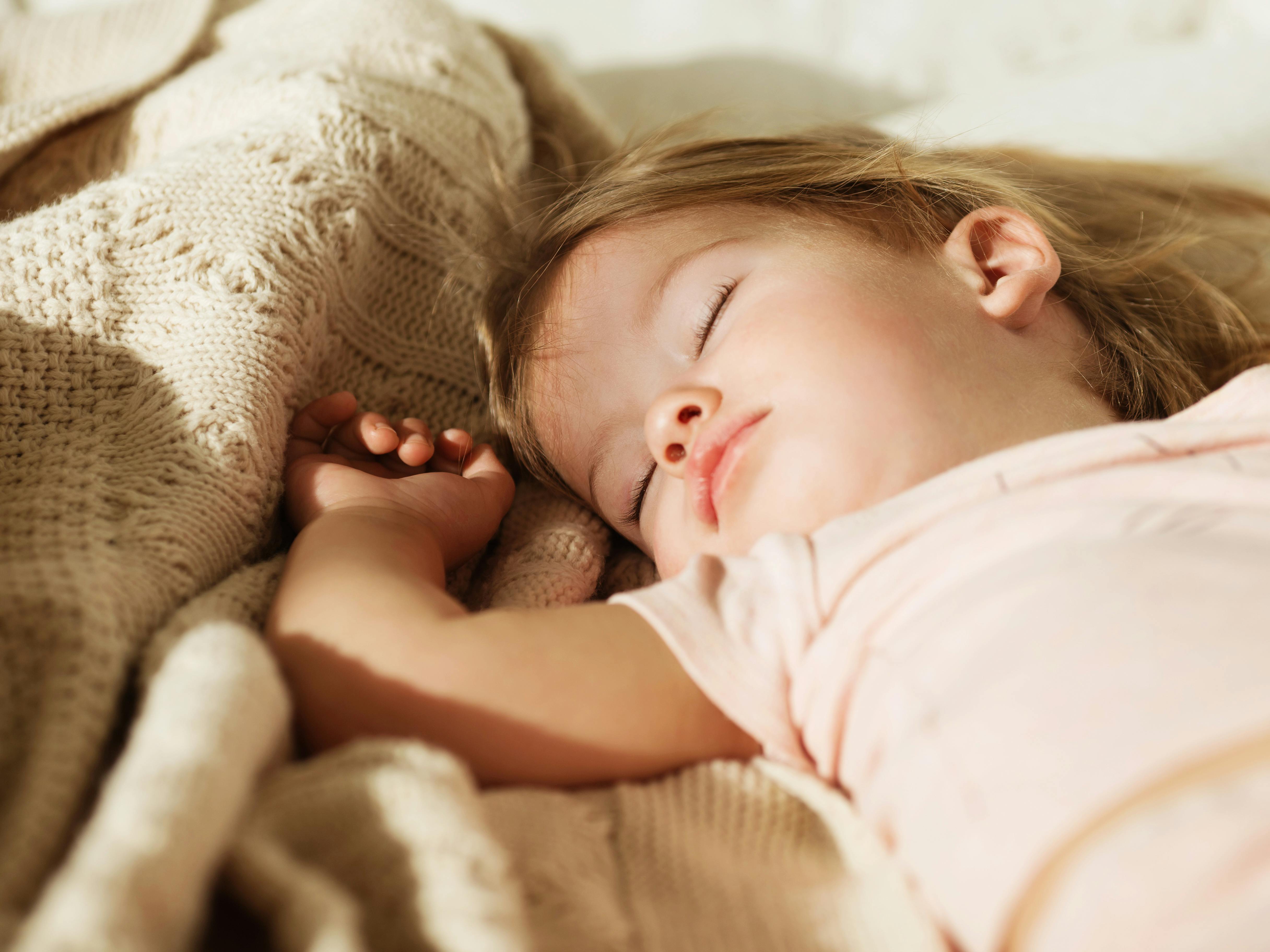 Sleeping little girl. Carefree sleep little baby with a soft toy on the bed. Close-up portrait of a beautiful sleeping child on knitted blanket. Sweet dreams
