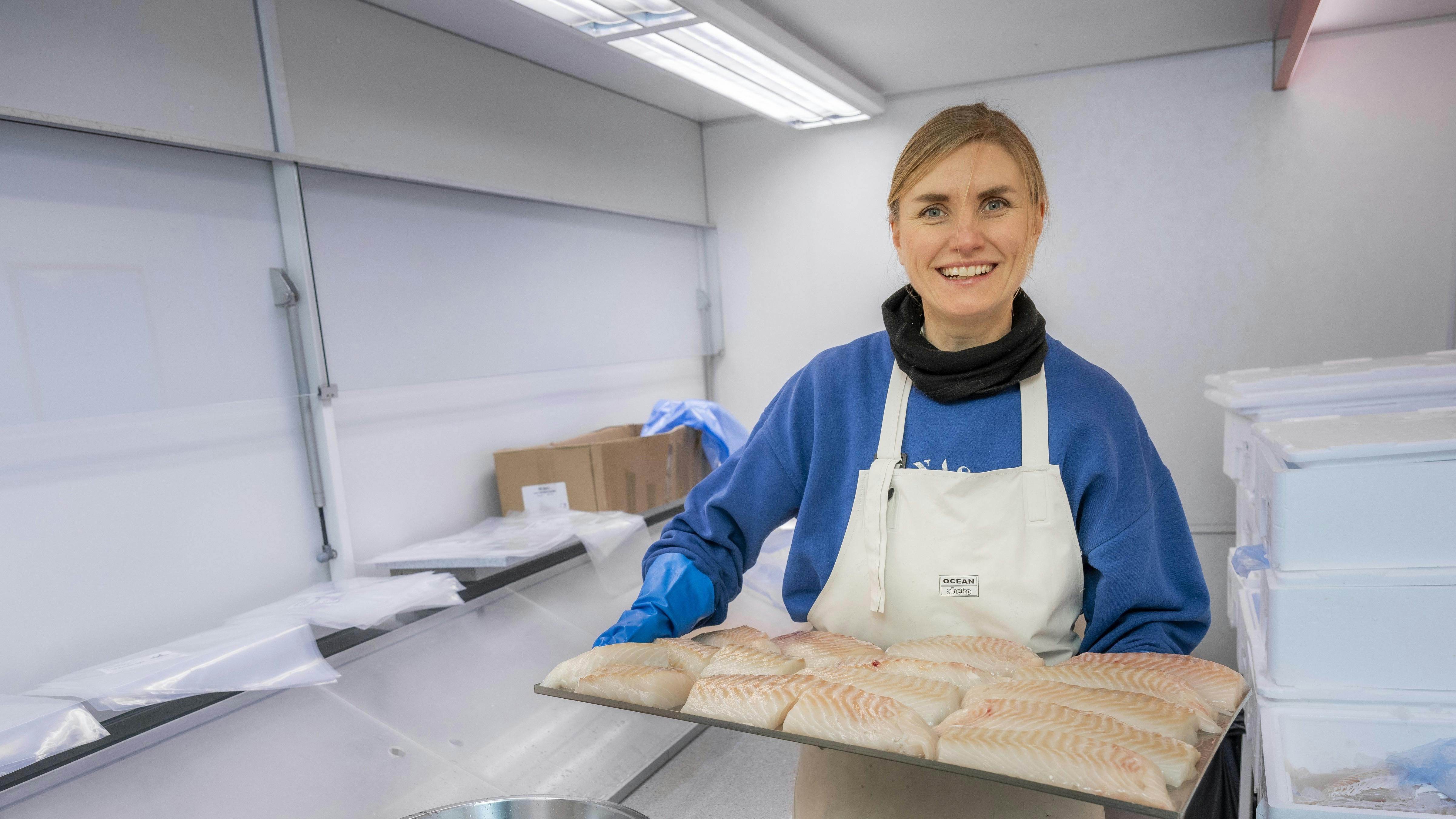 Anna står med en bakke med fisk i hænderne
