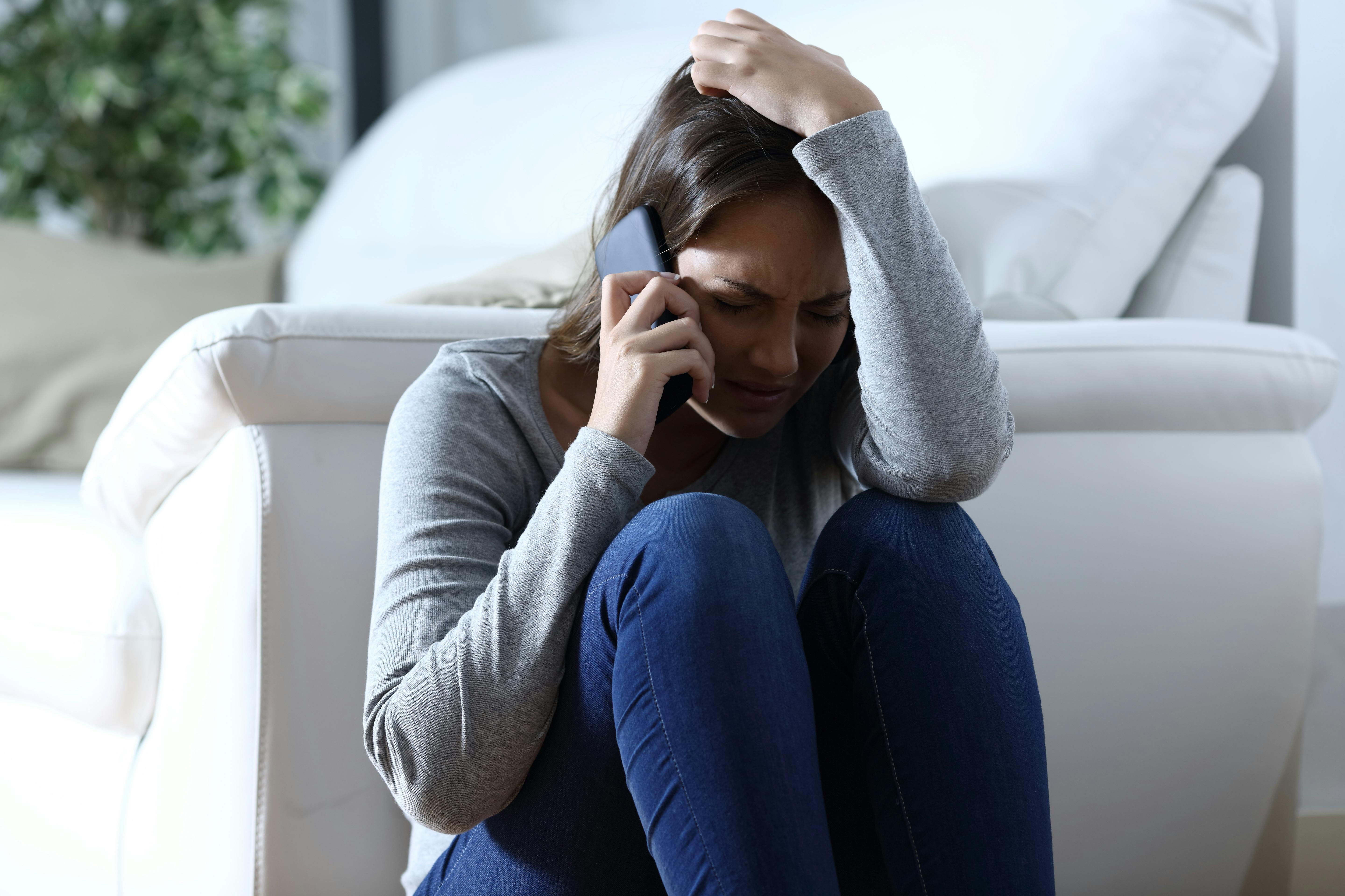 Sad woman complaining sitting on the floor talking on phone at home