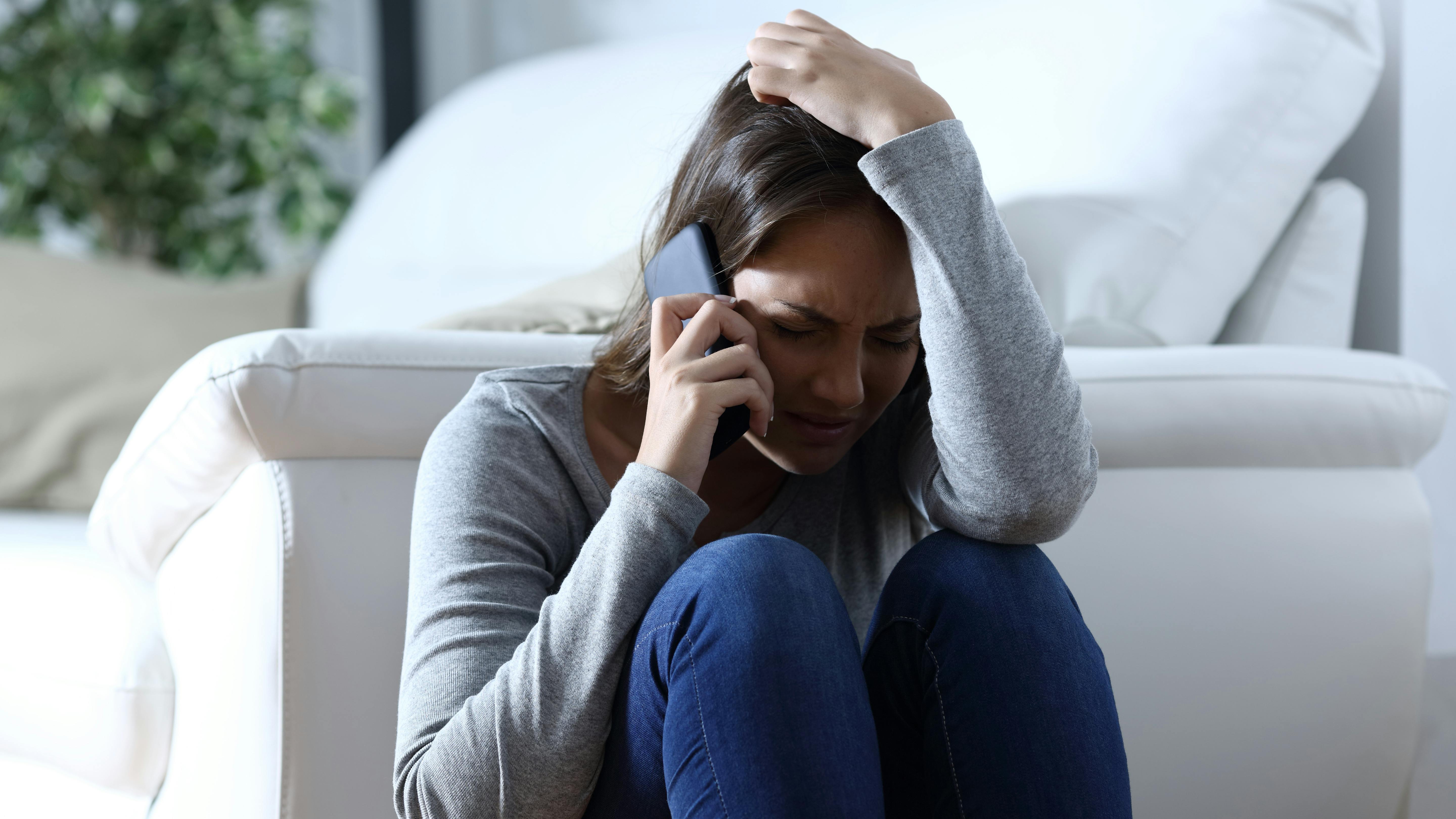 Sad woman complaining sitting on the floor talking on phone at home