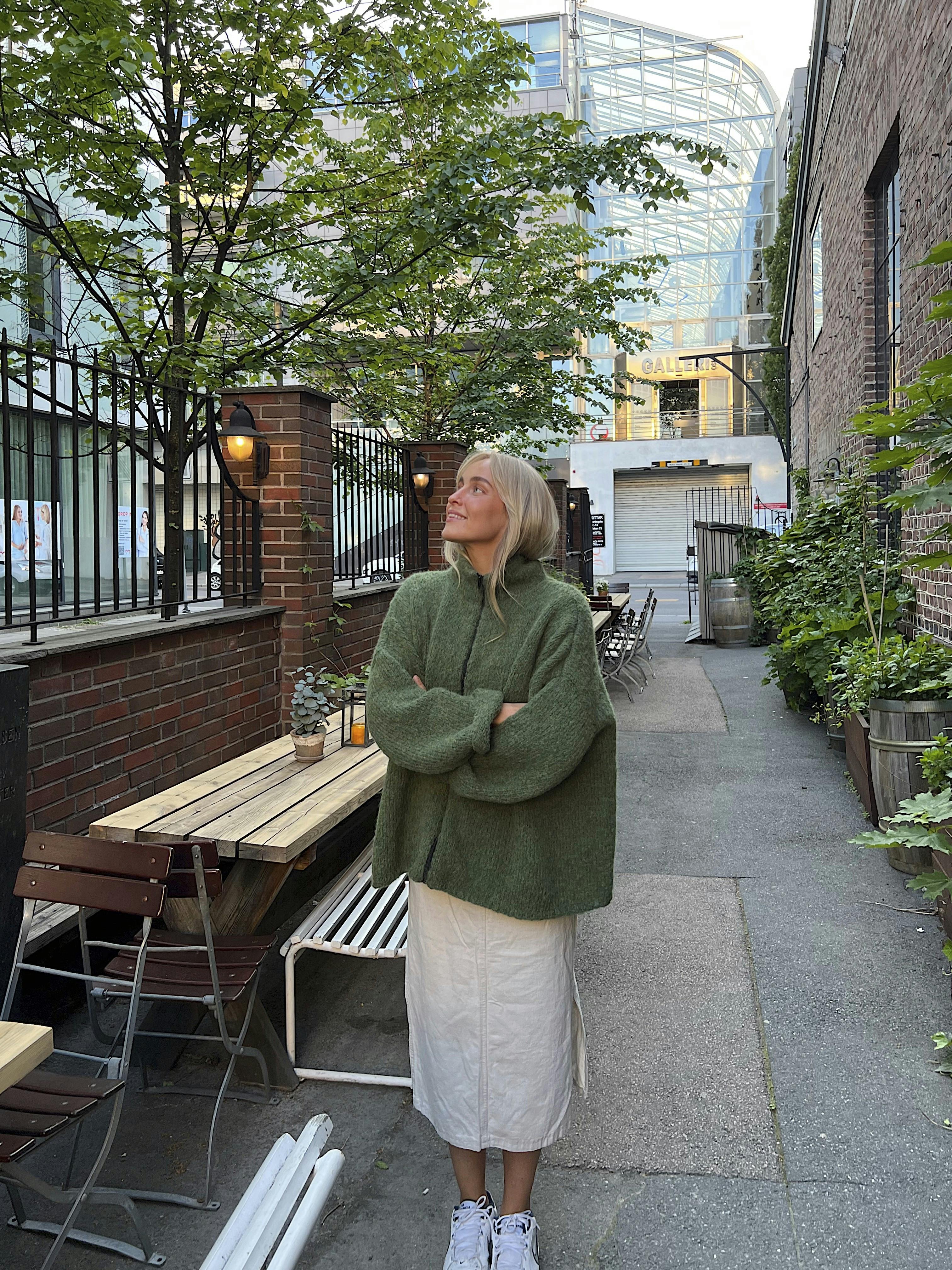 Kvinde der står i den grønne efterårs striktrøje, og kigger op mod himlen.