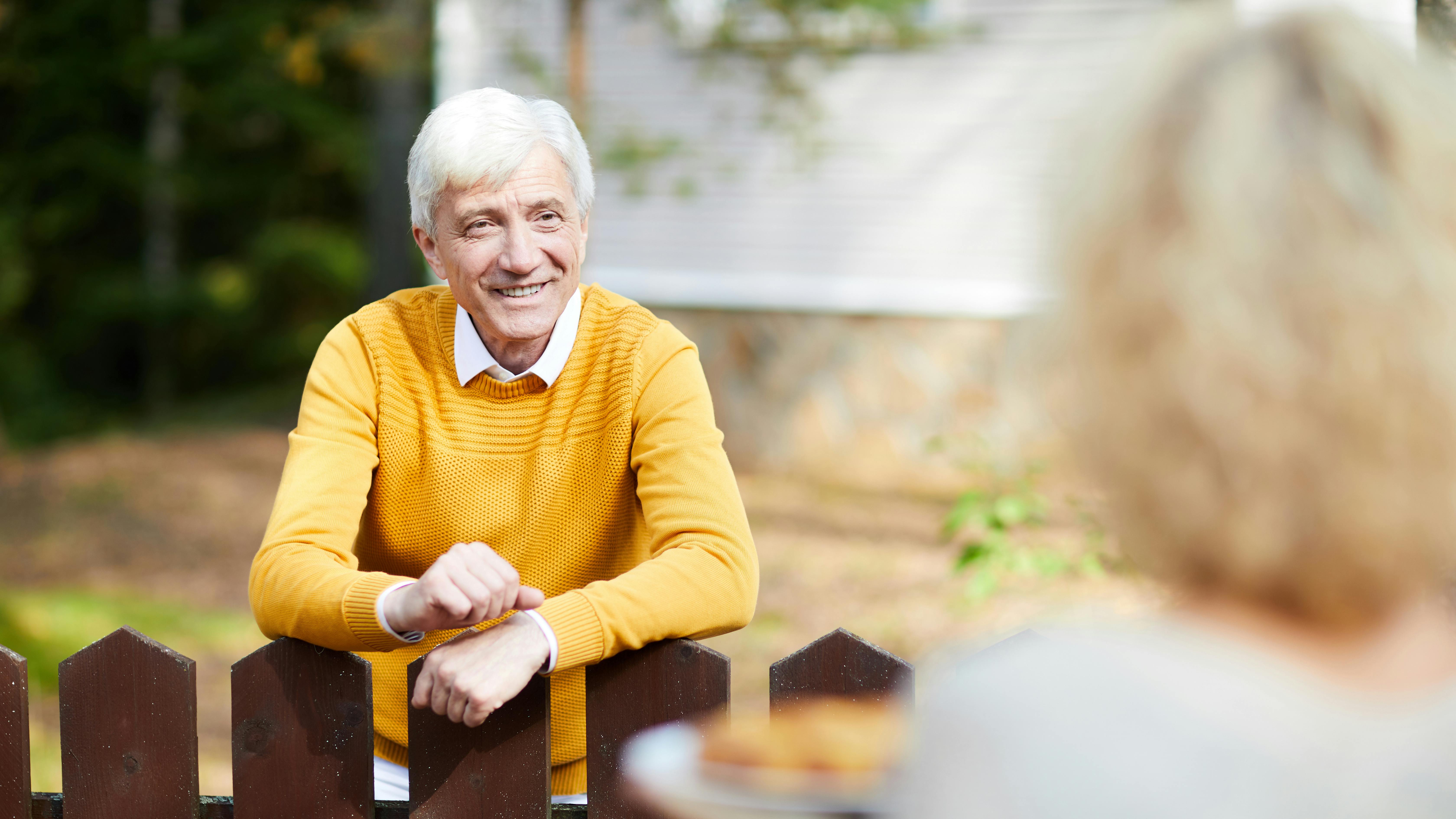 en ældre mand læner sig smilende ind over hegnet til naboen