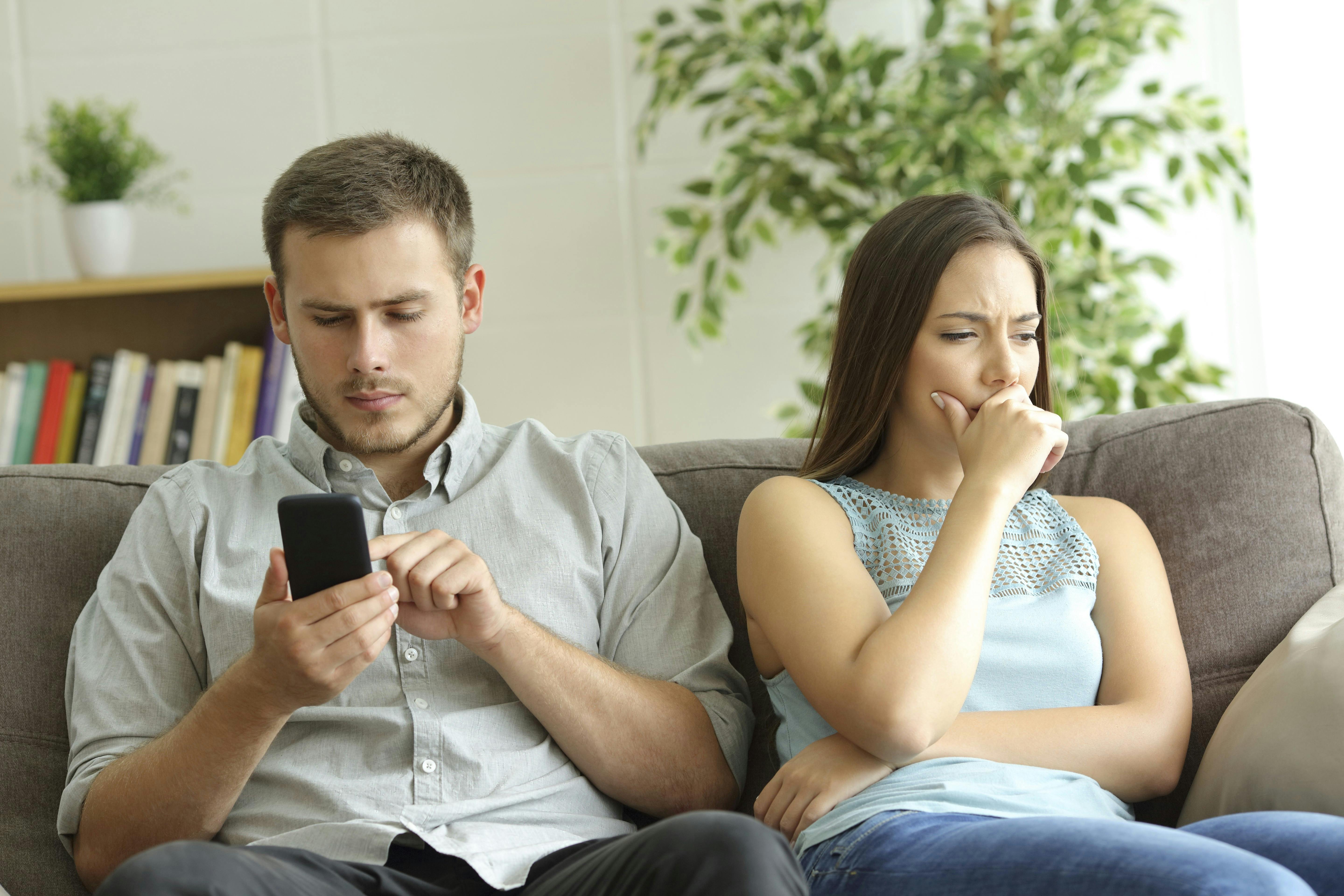 Mand kigger på sin telefon, mens konen sidder ved siden af