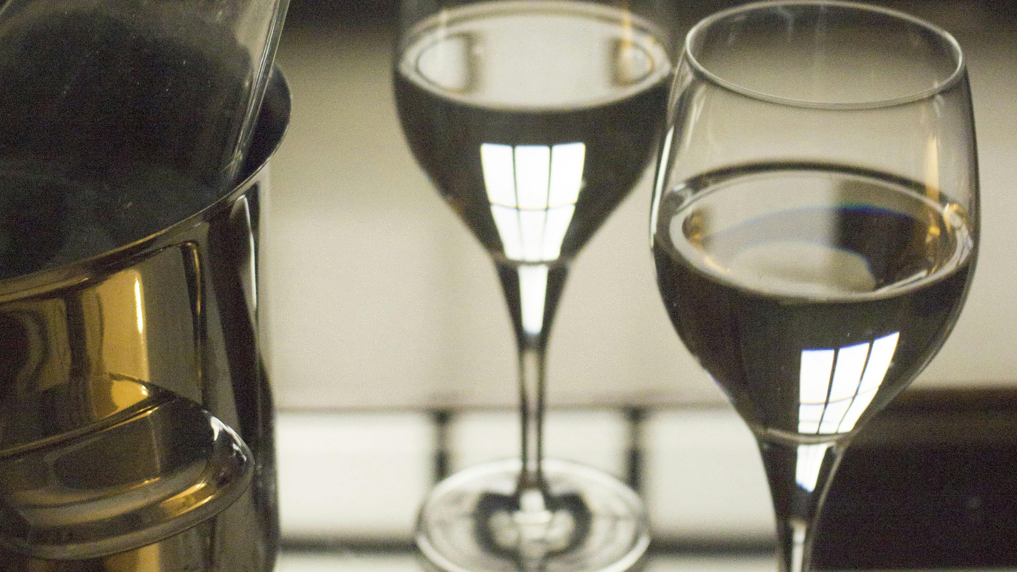 Glass water bottle open, metal ice bucket and two glasses on glass coffee table in room with glass door behind defocused. Monochrome vertical color digital photograph.