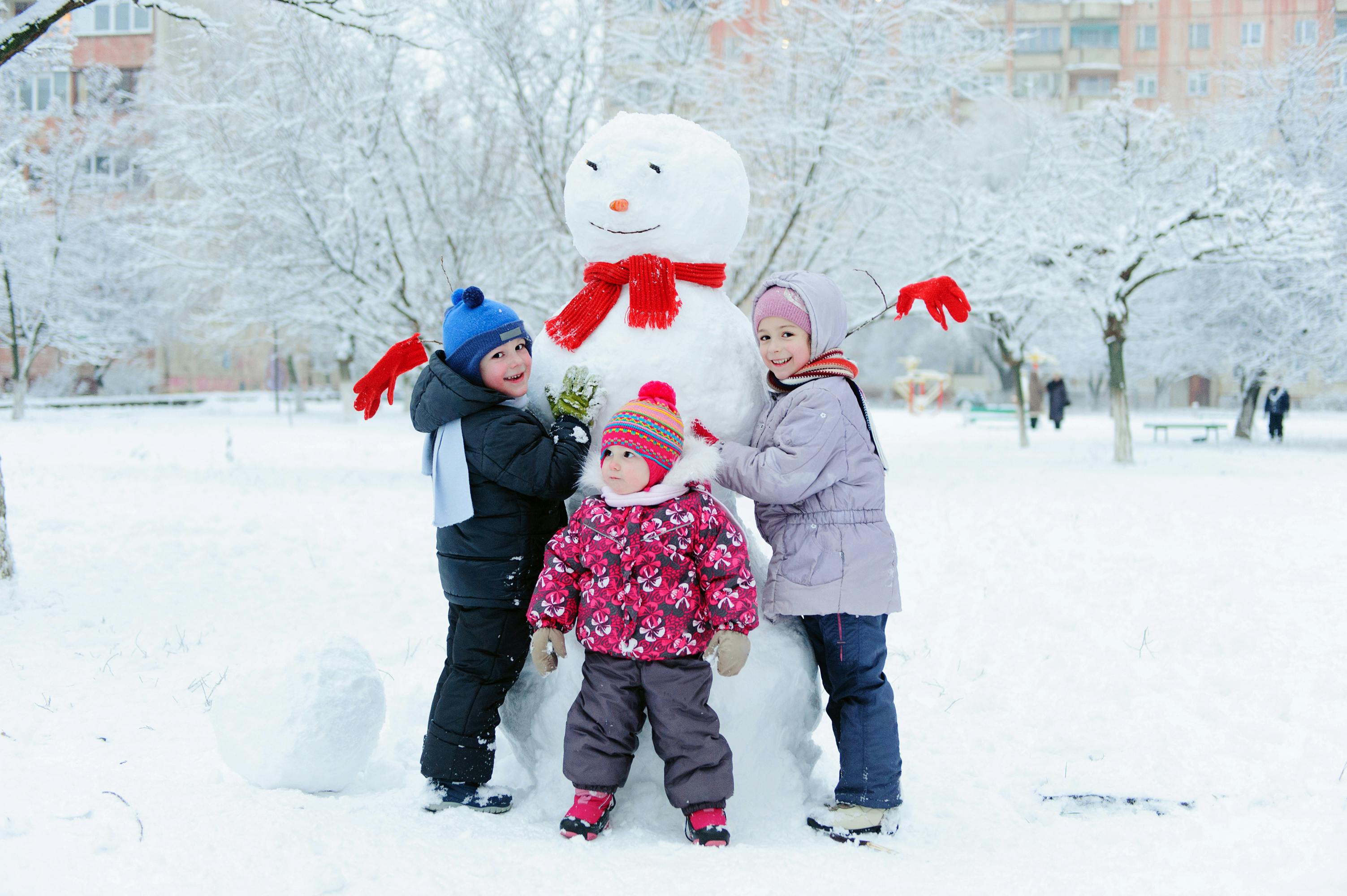 Happy beautiful children building snowman in garden