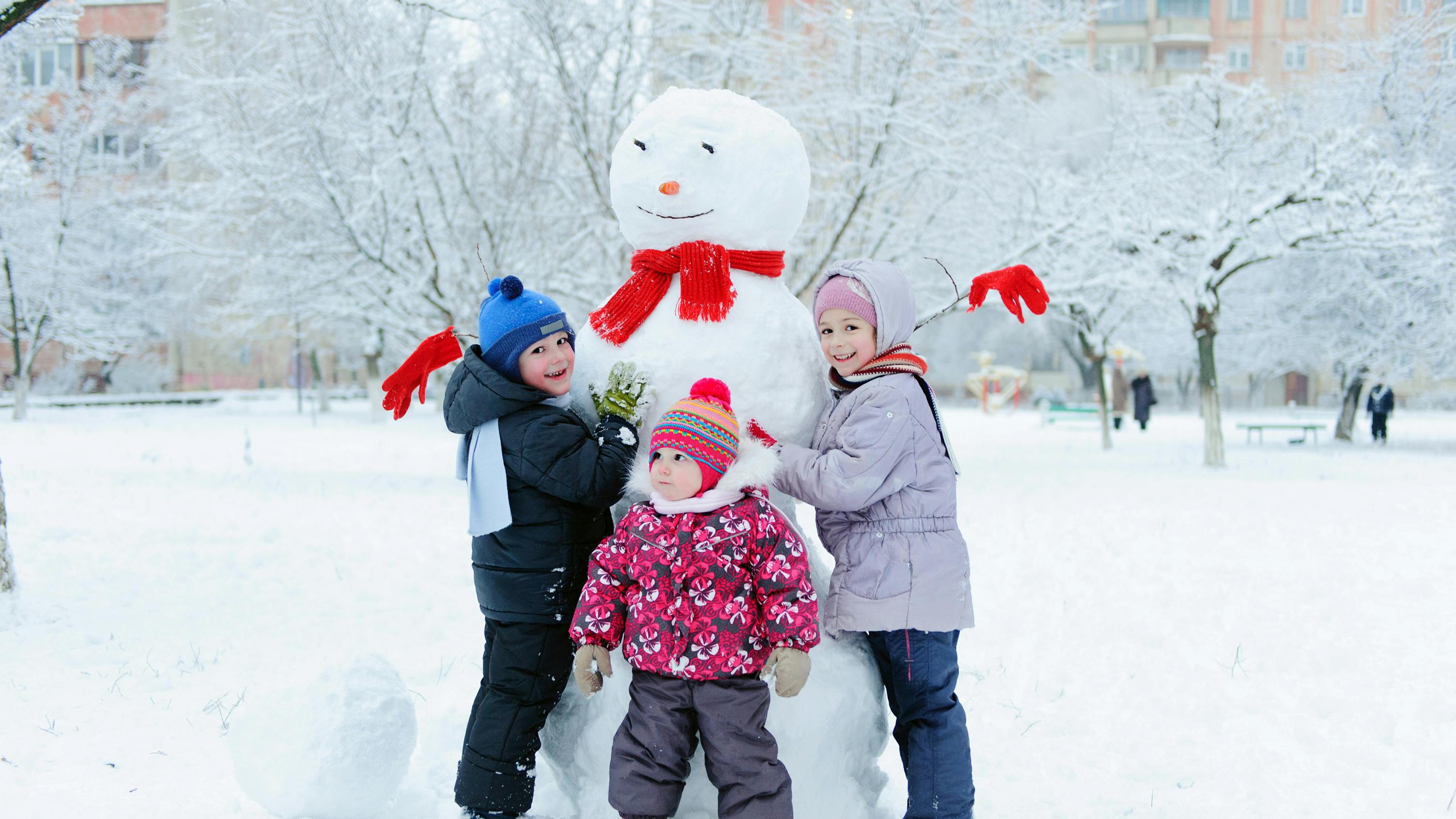 Happy beautiful children building snowman in garden