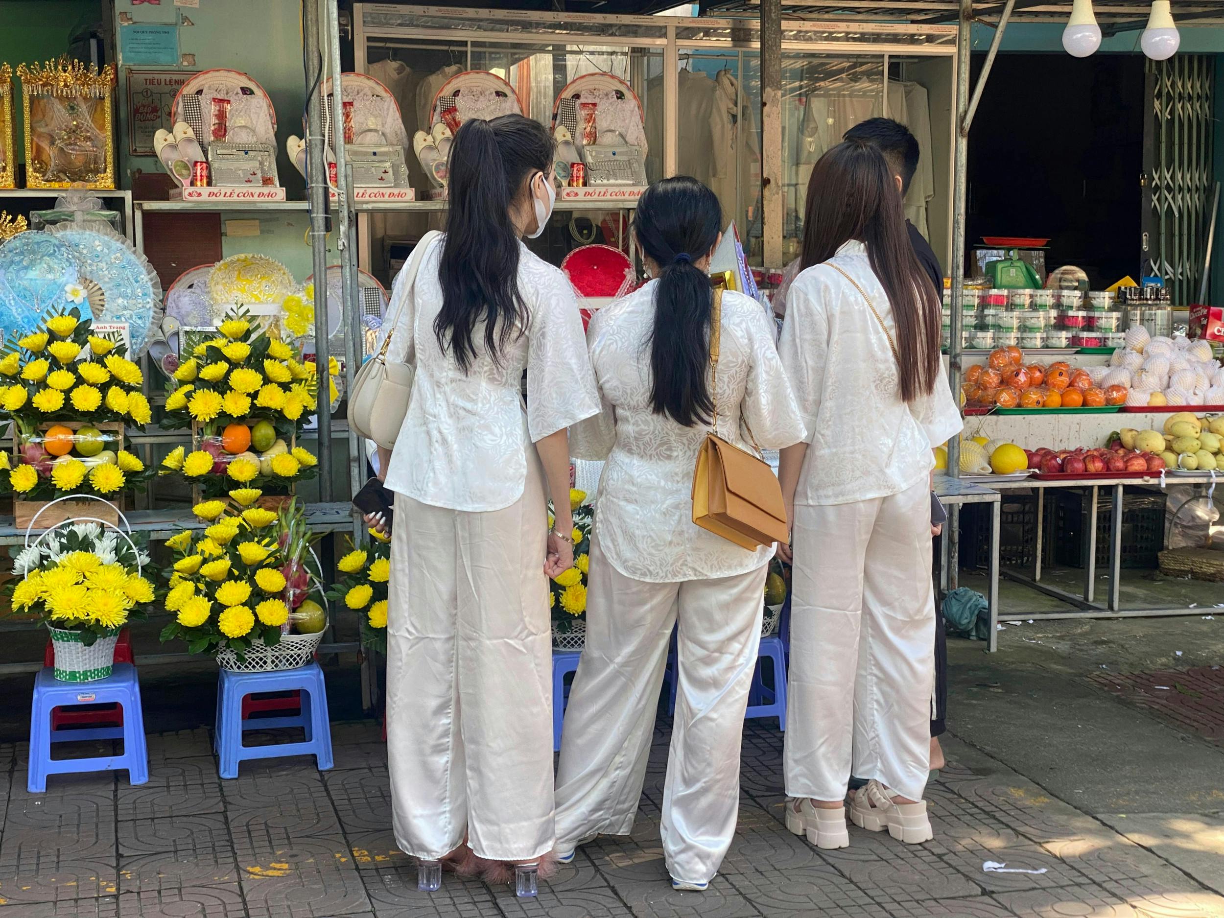 Kvinder i festtøj kigger på blomsteropsatser på Con Dao Market.