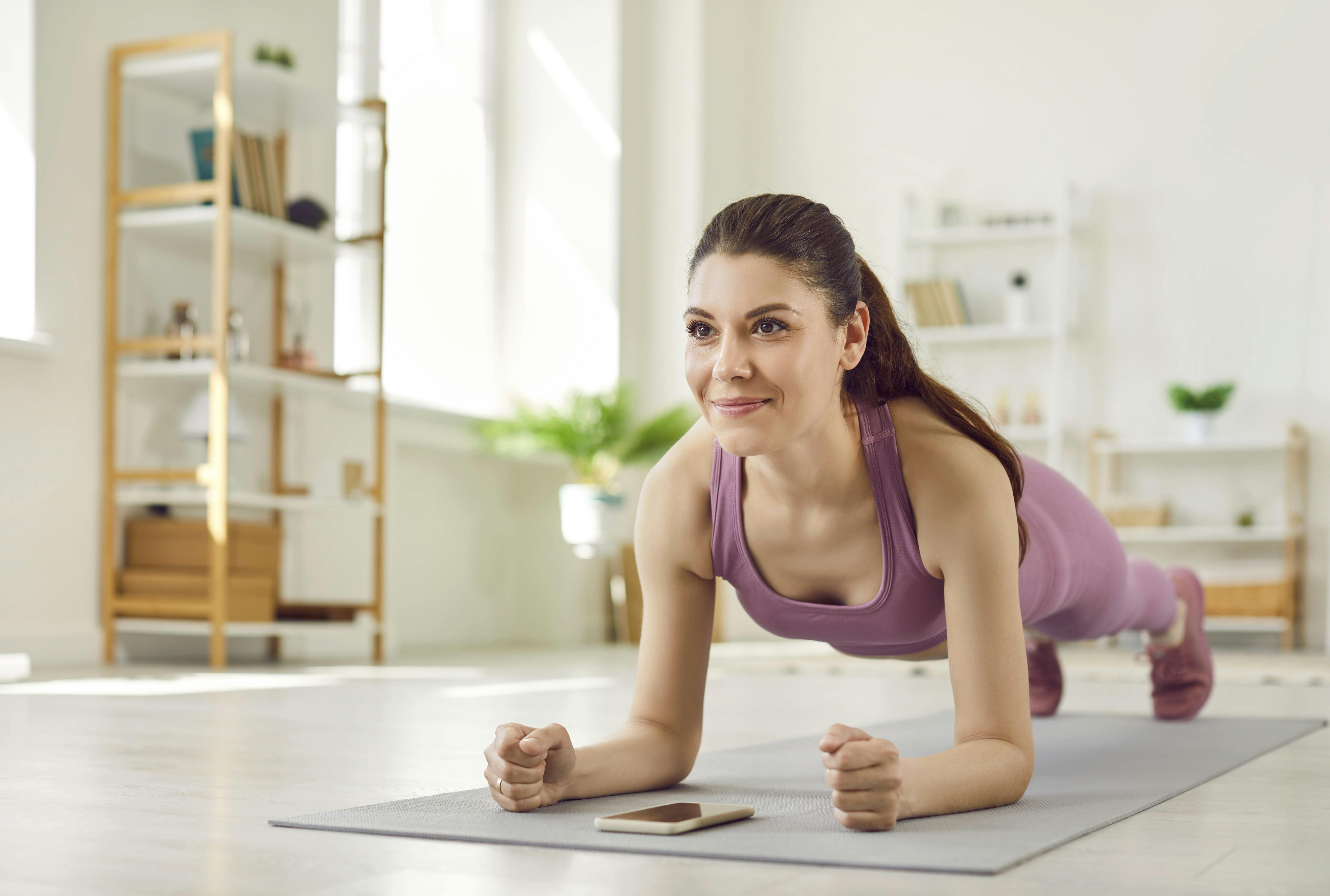 Portrait of a young attractive sporty woman doing plank sport exercise lying on yoga mat on the floor in the living room at home. Fitness, fit, workout sport and home training concept.