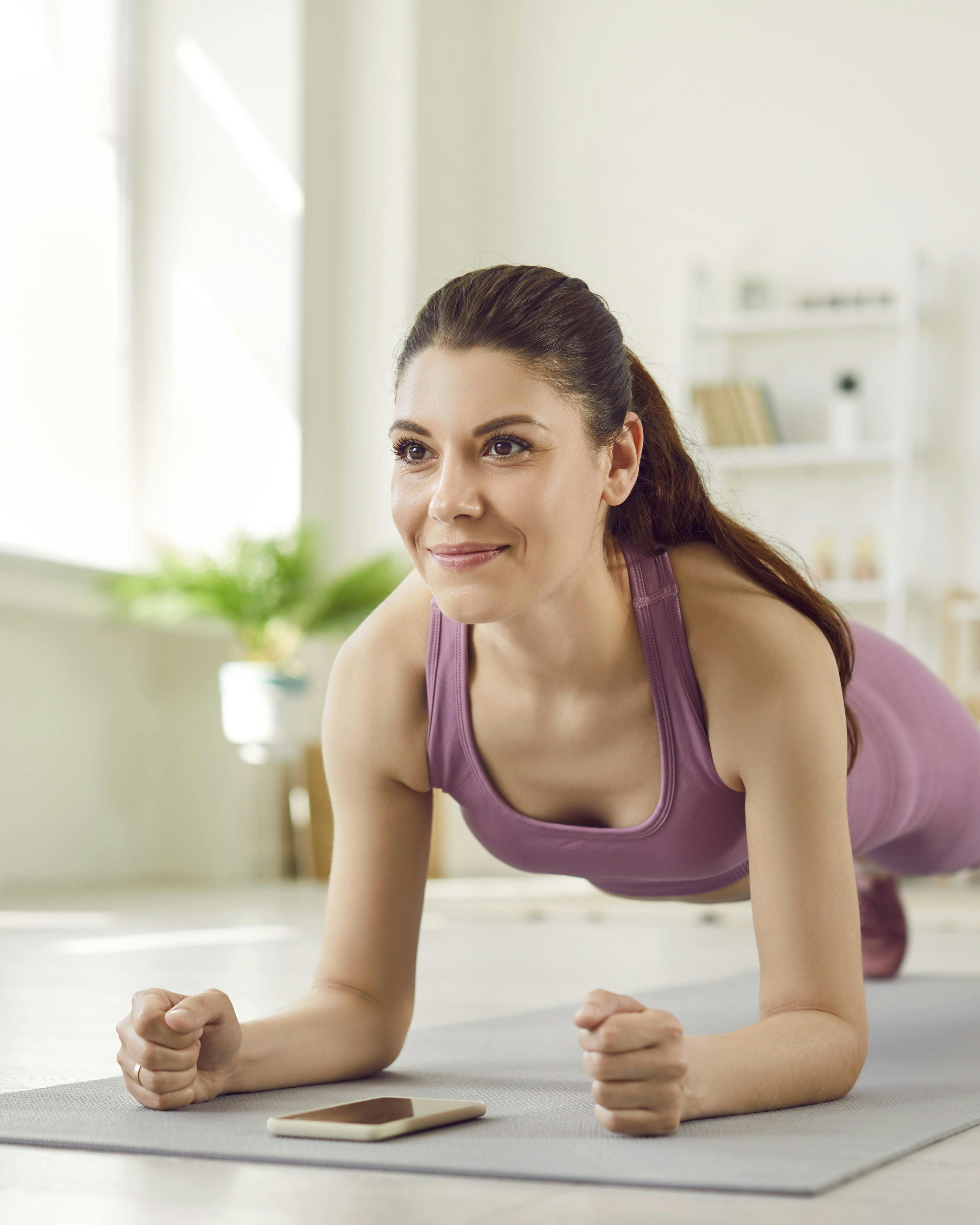 Portrait of a young attractive sporty woman doing plank sport exercise lying on yoga mat on the floor in the living room at home. Fitness, fit, workout sport and home training concept.