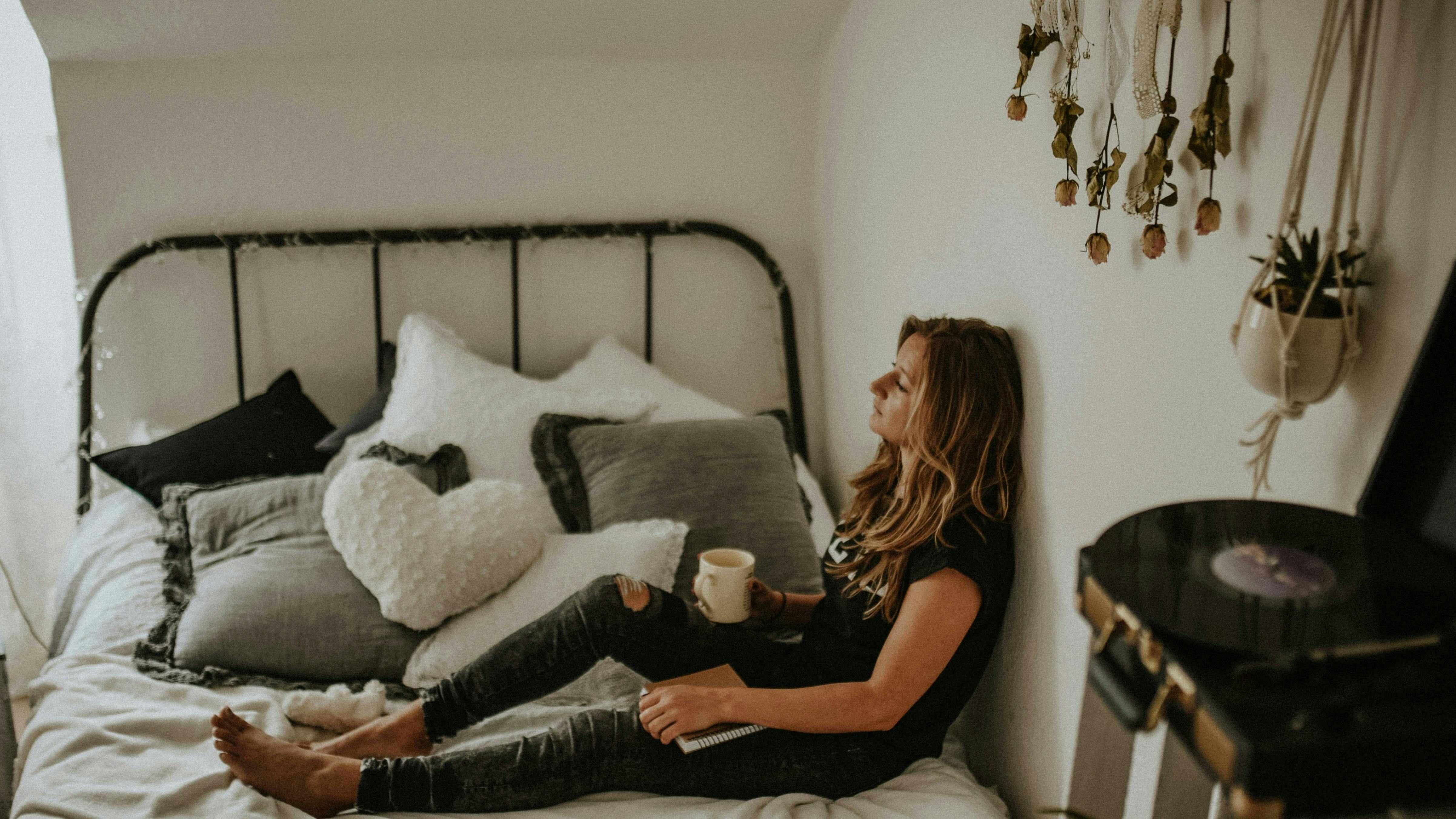 Kvinde sidder på en seng og ser opgivende ud.