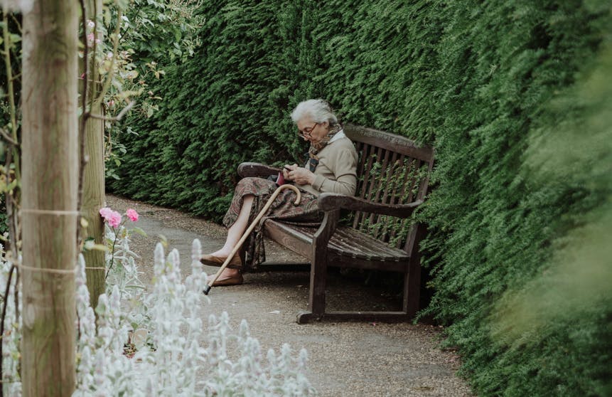 Ældre dame, der sidder på en bænk på en kirkegård.