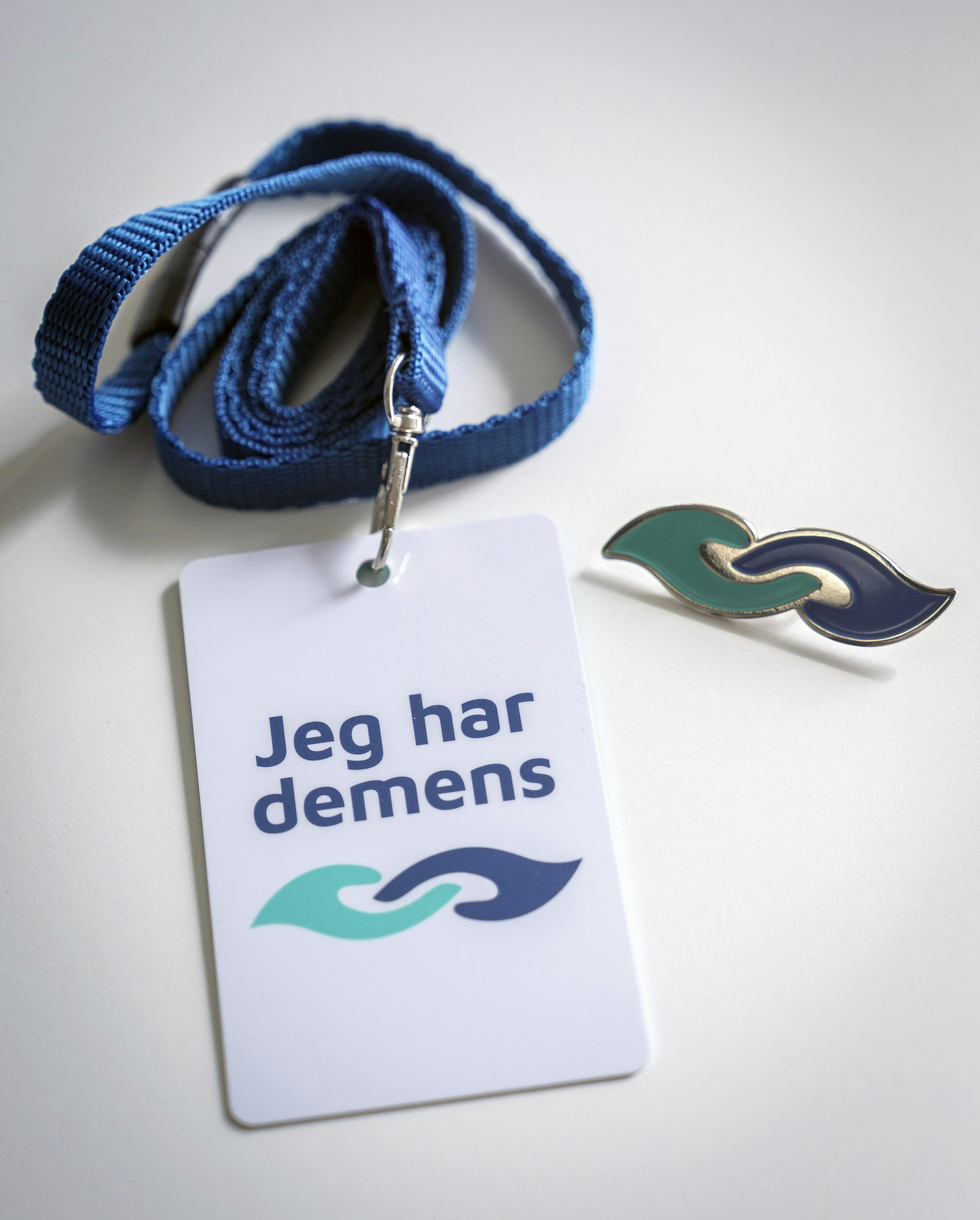 Det nationale demenssymbol viser to hænder, der rækker ud mod hinanden. Bæreren af symbolet kan have brug for ekstra hjælp, så tag gerne kontakt, tal tydeligt og vær tålmodig.