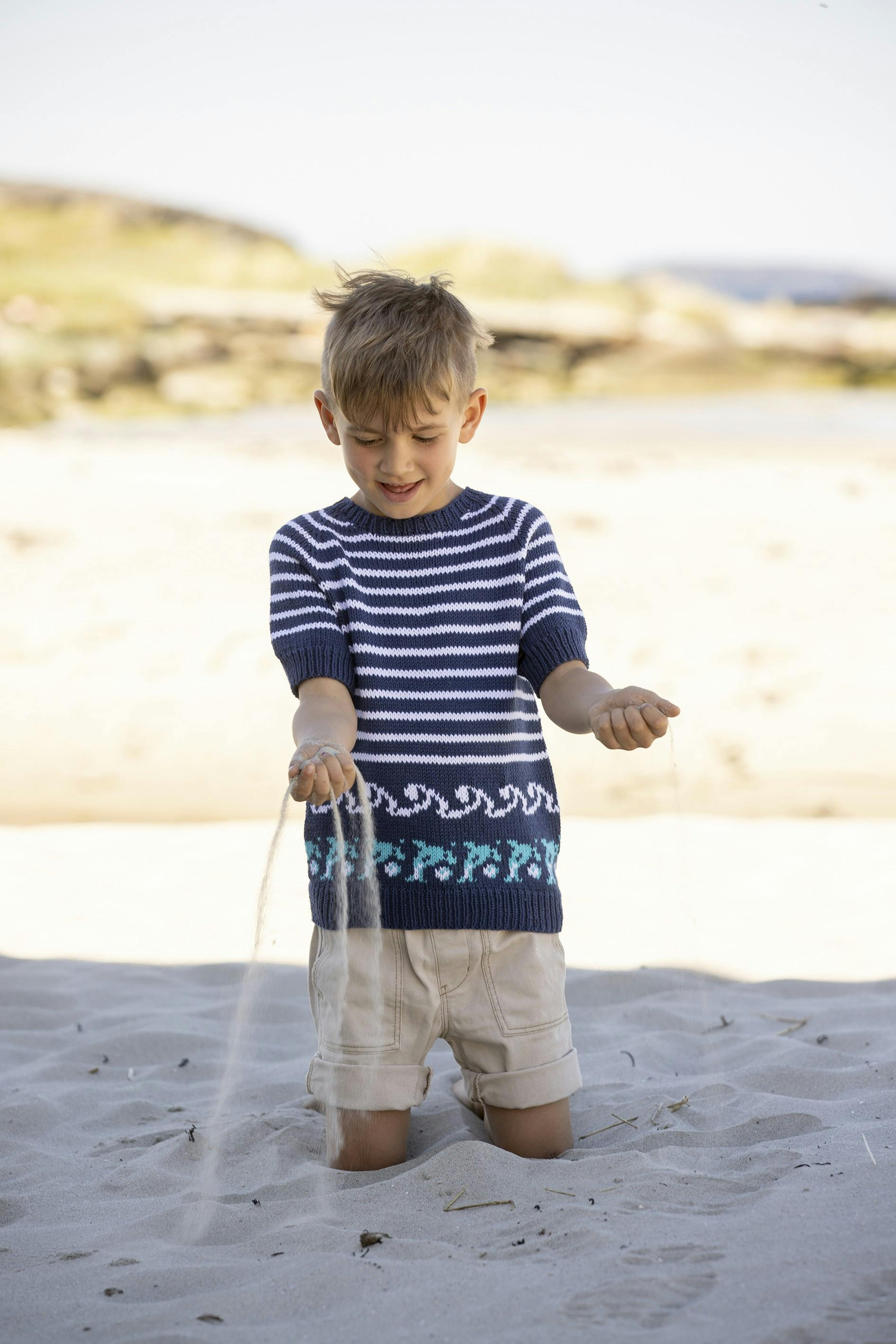 T-shirt med delfiner, mens en dreng leger i sandet.