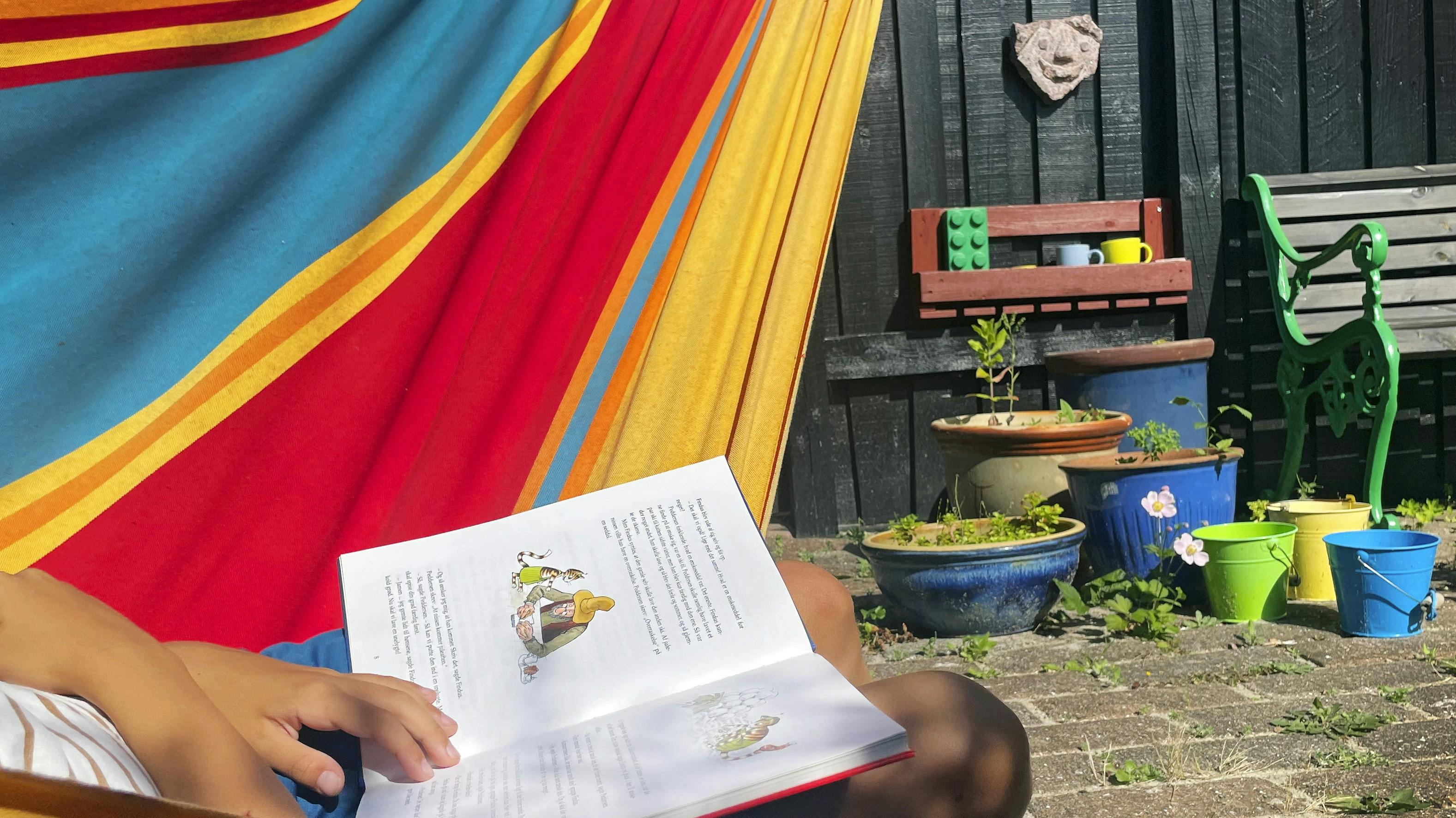 Barn der sidder i en hængekøje, og læser i en bog.
