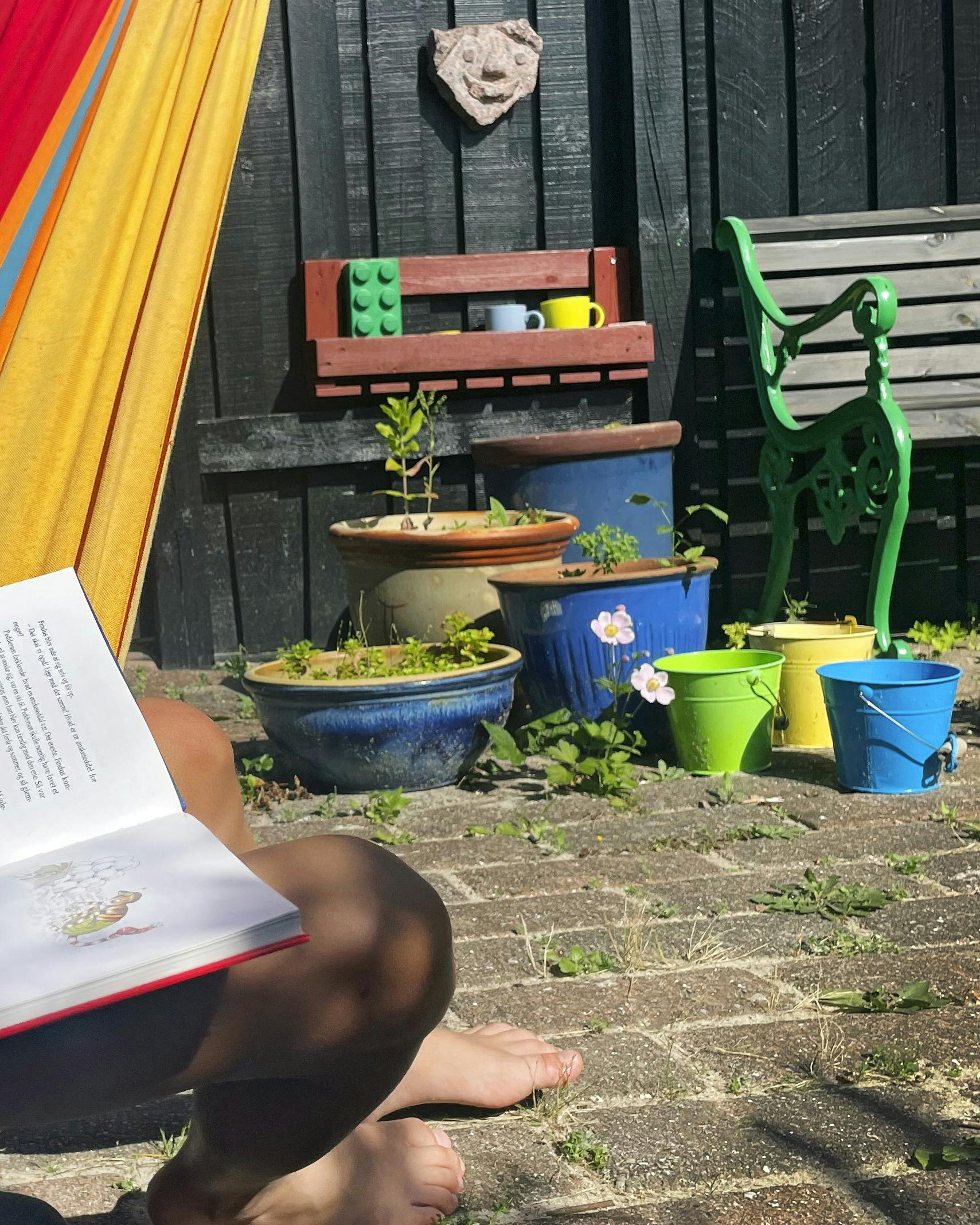 Barn der sidder i en hængekøje, og læser i en bog.