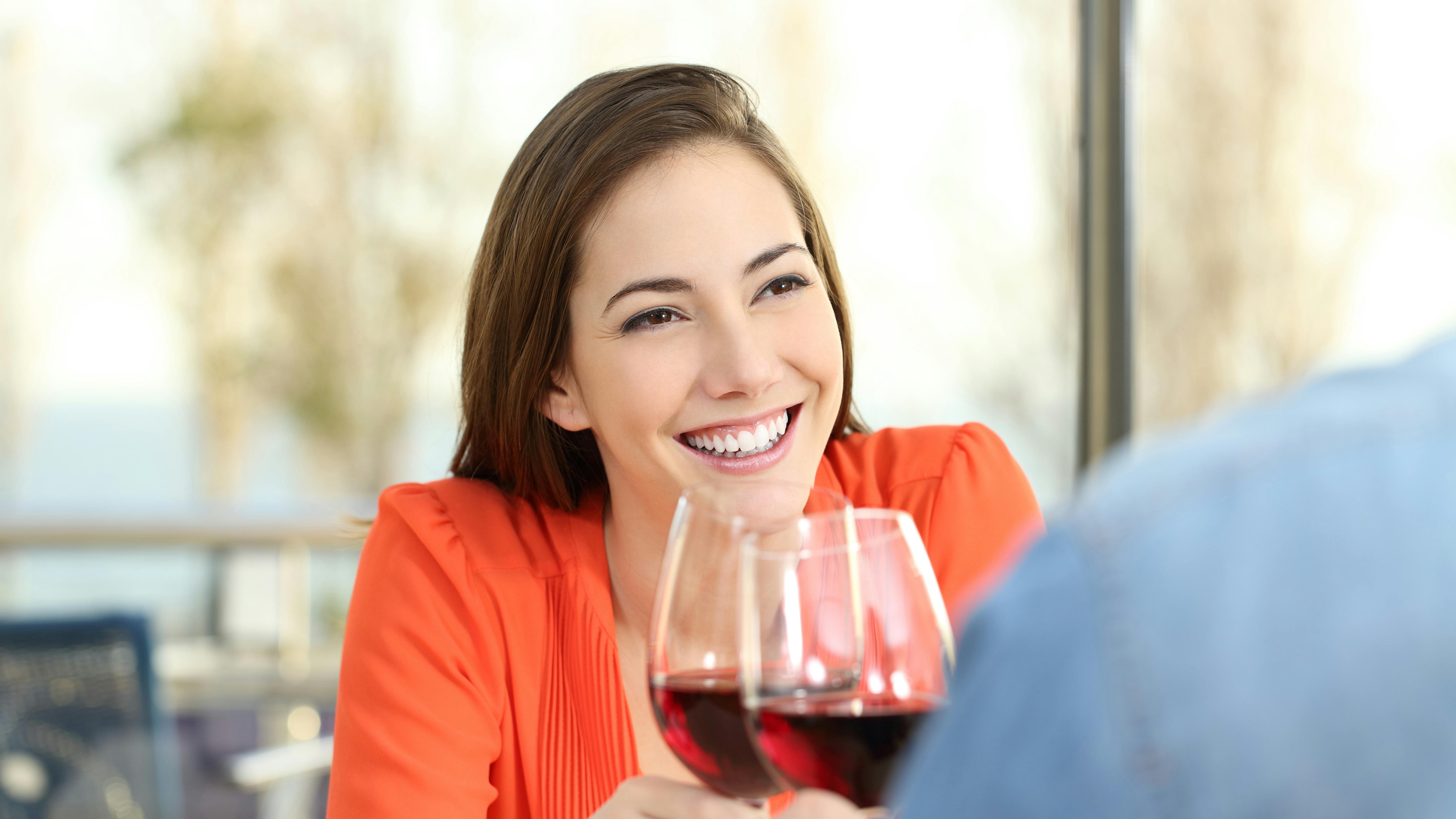 Glad kvinde sidder foran mand og skåler med et glas rødvin