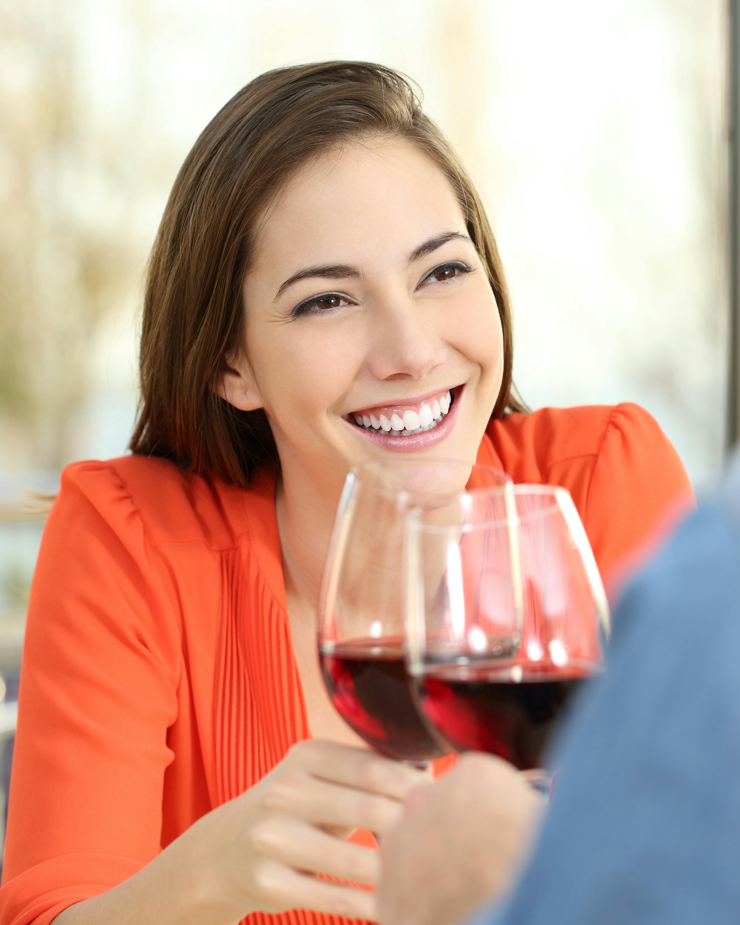 Glad kvinde sidder foran mand og skåler med et glas rødvin