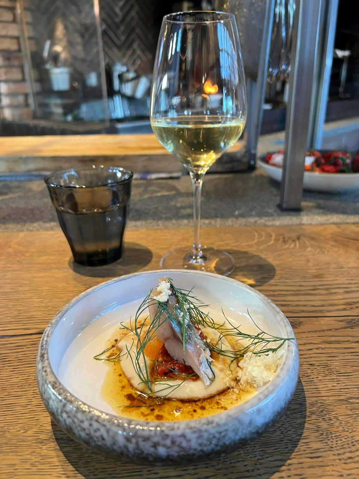 En tallerken med makrel og et glas vin.