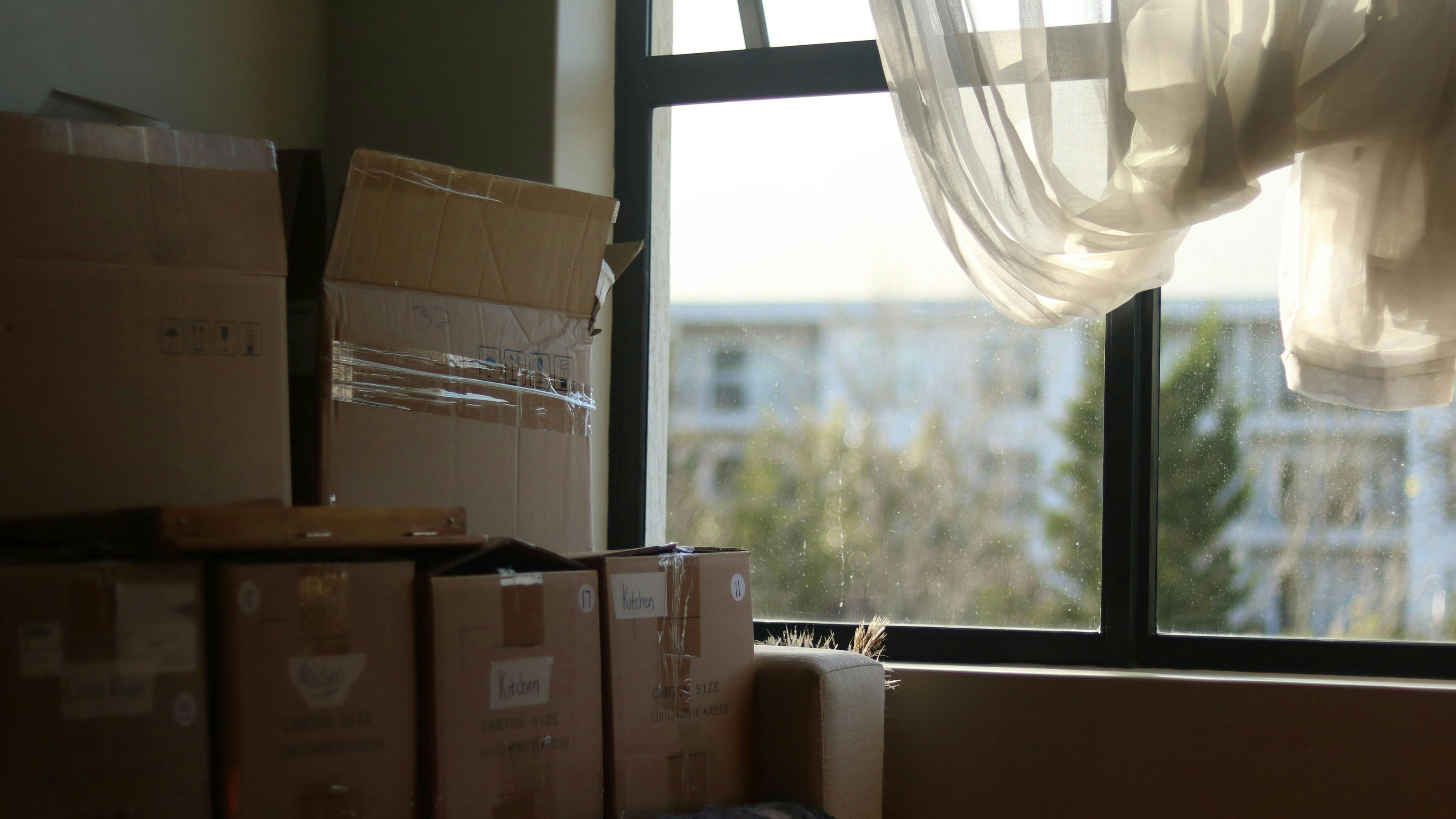 En stabel flyttekasser står op ad et vindue.