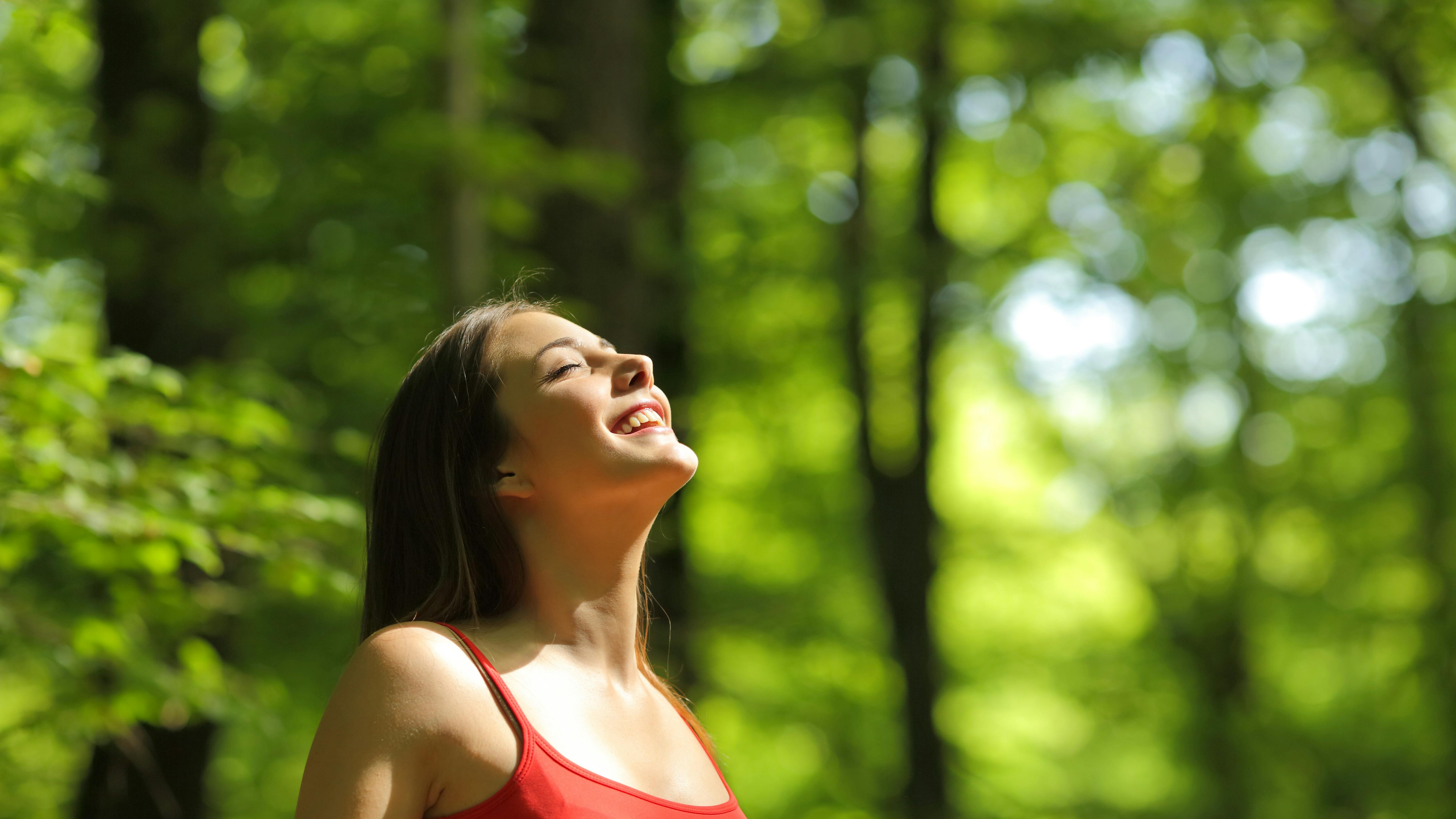 Kvinde i rød undertrøje trækker frisk luft i skoven