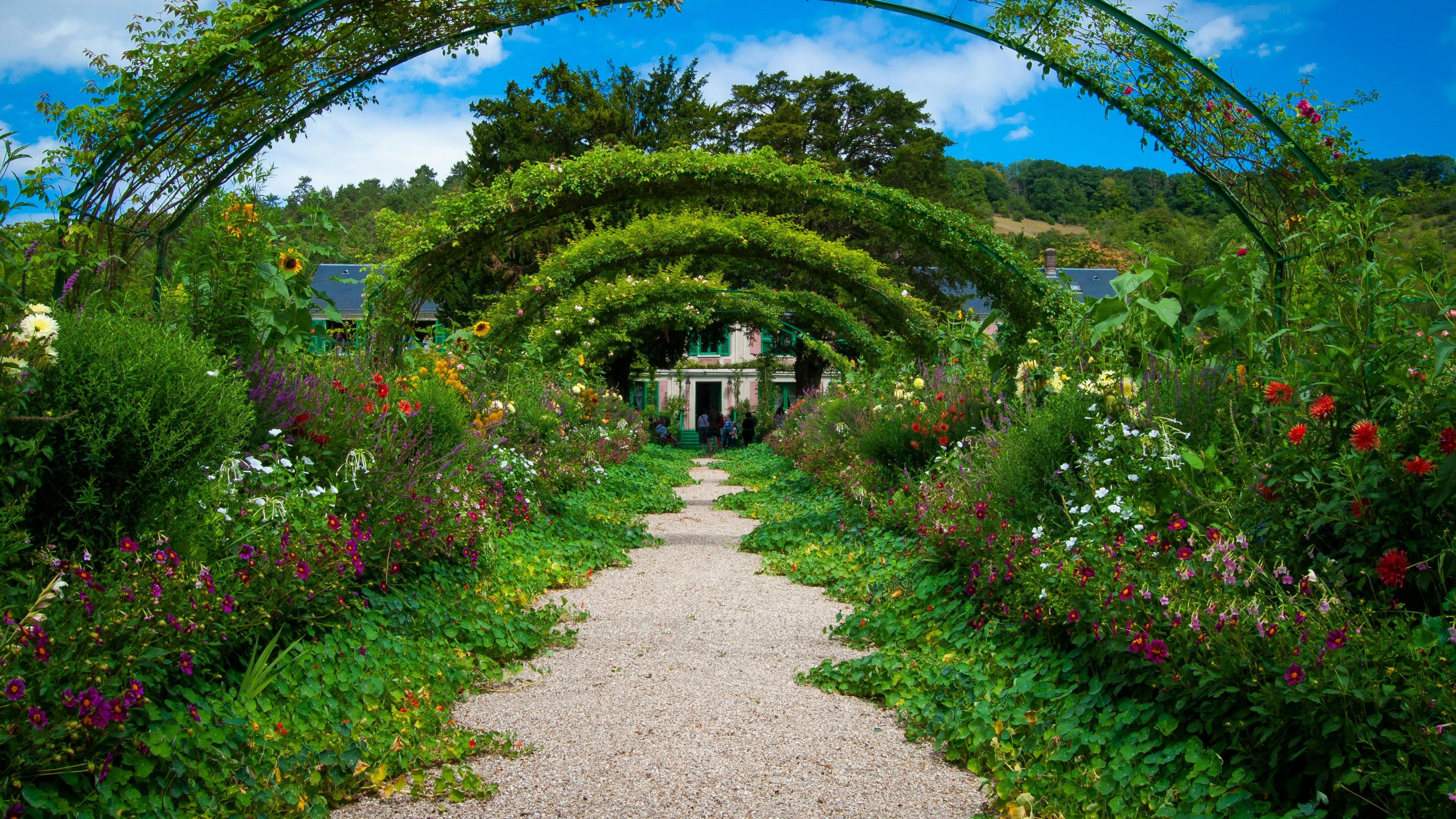 Stor blomsterhave med blomsterbuer og grussti i midten.