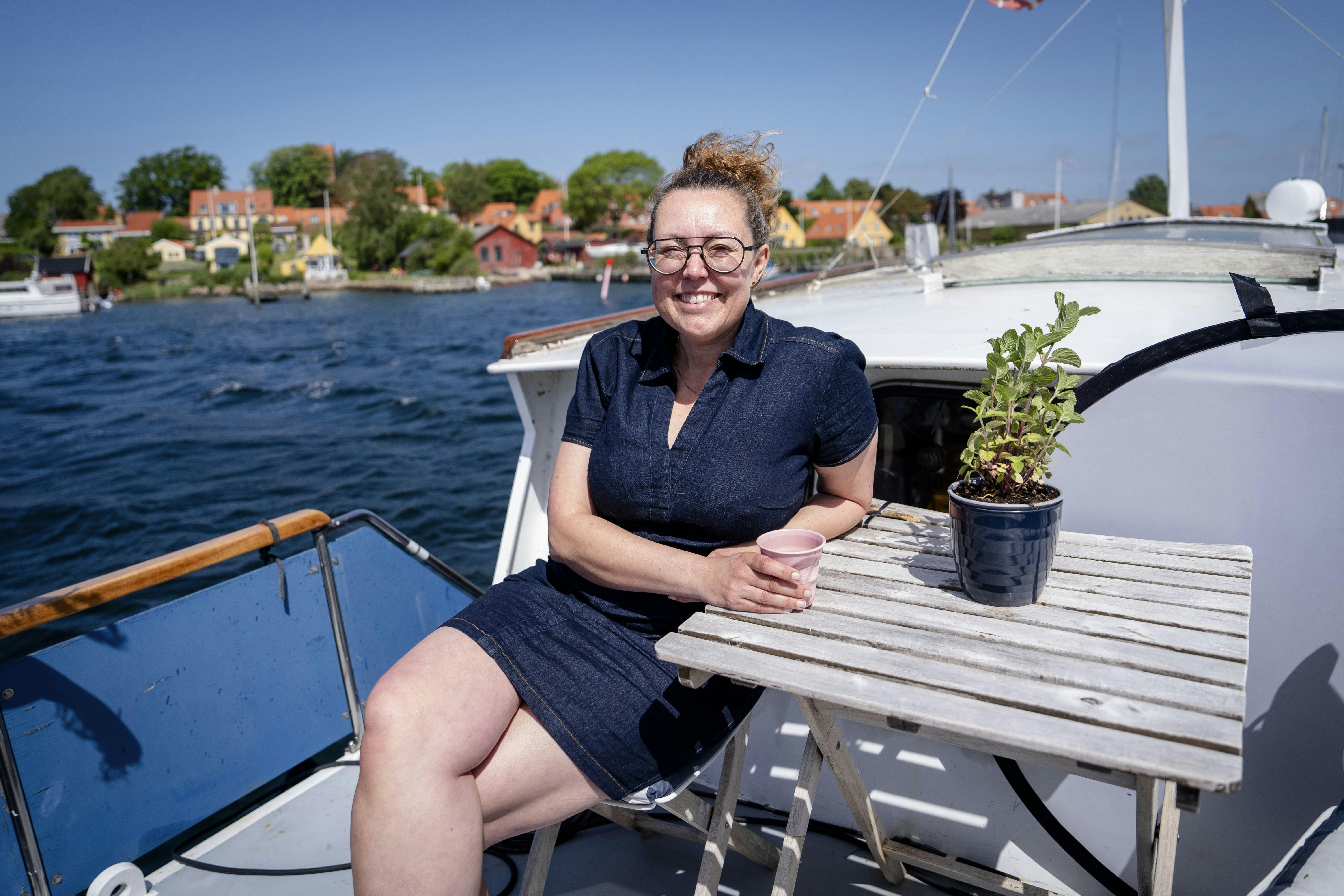 Linda Kristiansen sidder i solen på dækket af sin båd, som hun bor på.
