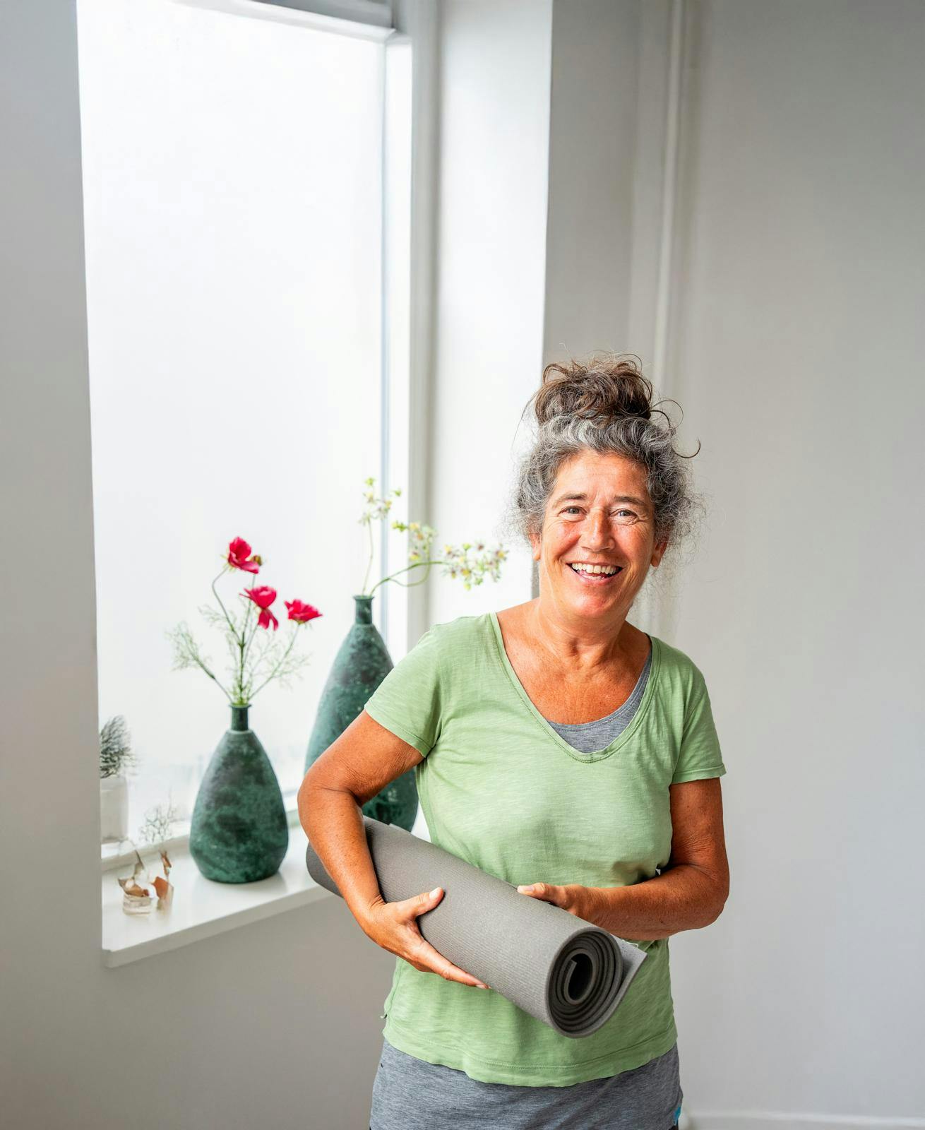 Ældre kvinde, der står med en sammenrullet yogamåtte i hænderne.