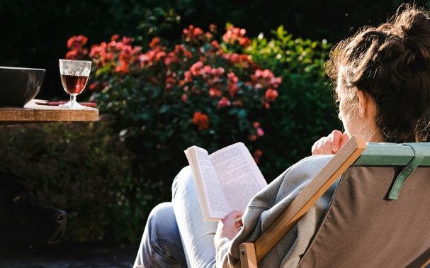 Kvinde, der sidder i en liggestol i haven og læser. 