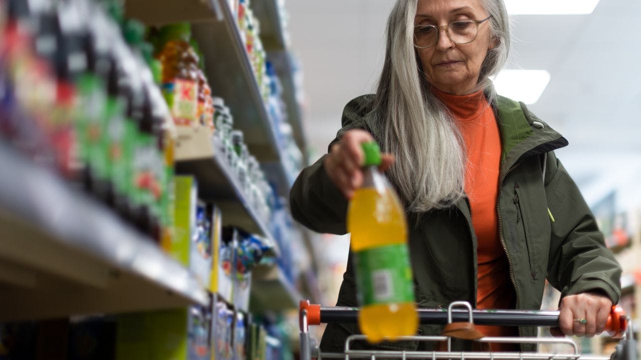 Ældre kvinder lægger en sodavand i sin vogn i supermarkedet