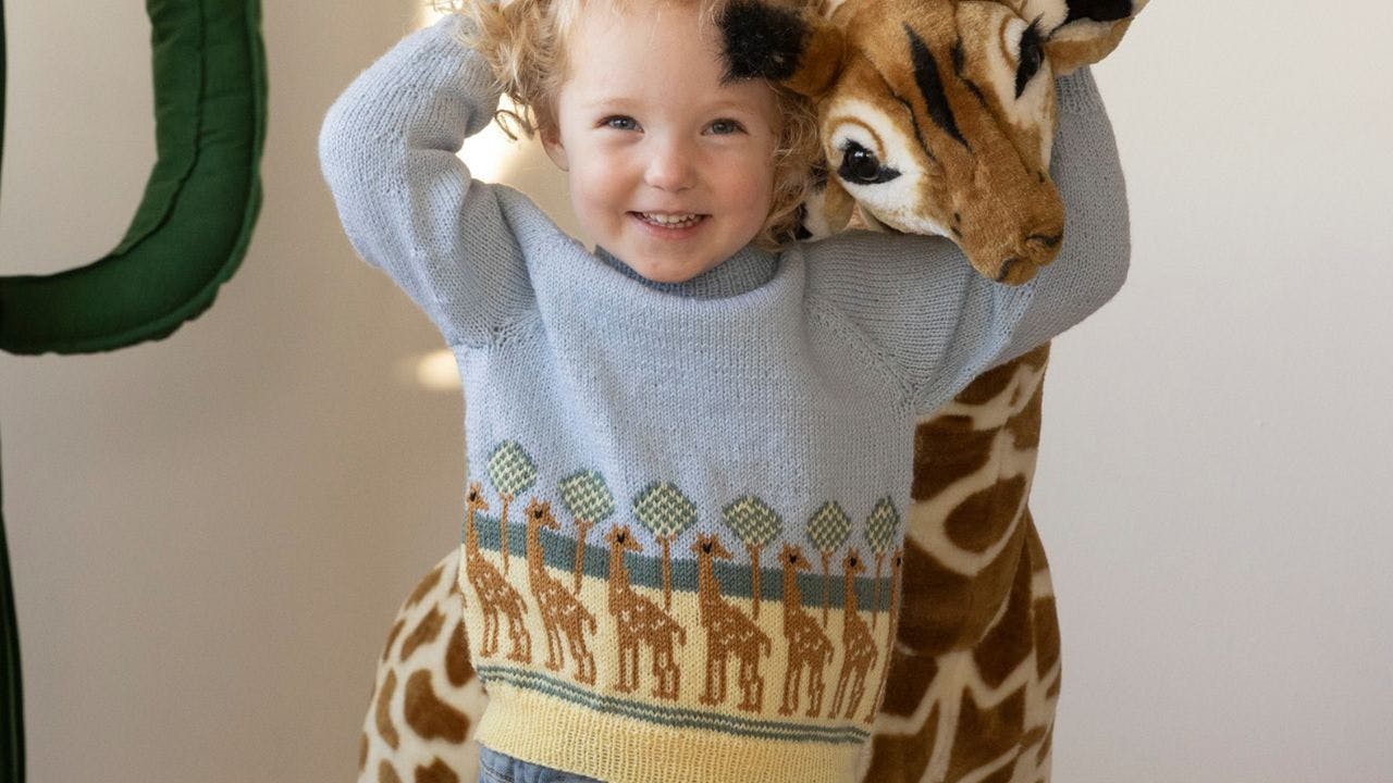 Barn står foran girafbamse iført en sweater med giraffer