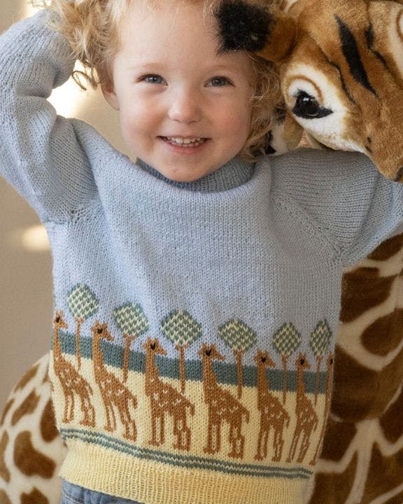 Barn står foran girafbamse iført en sweater med giraffer