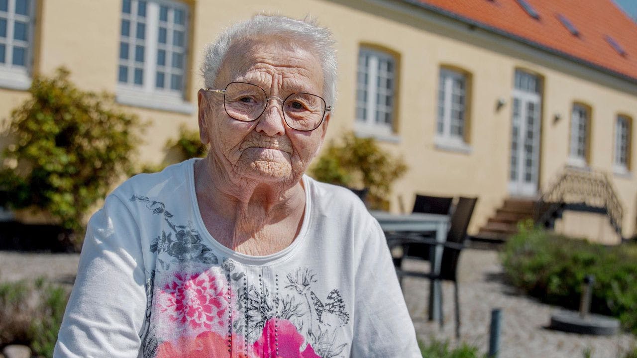 Ældre kvinde står foran gult hus 