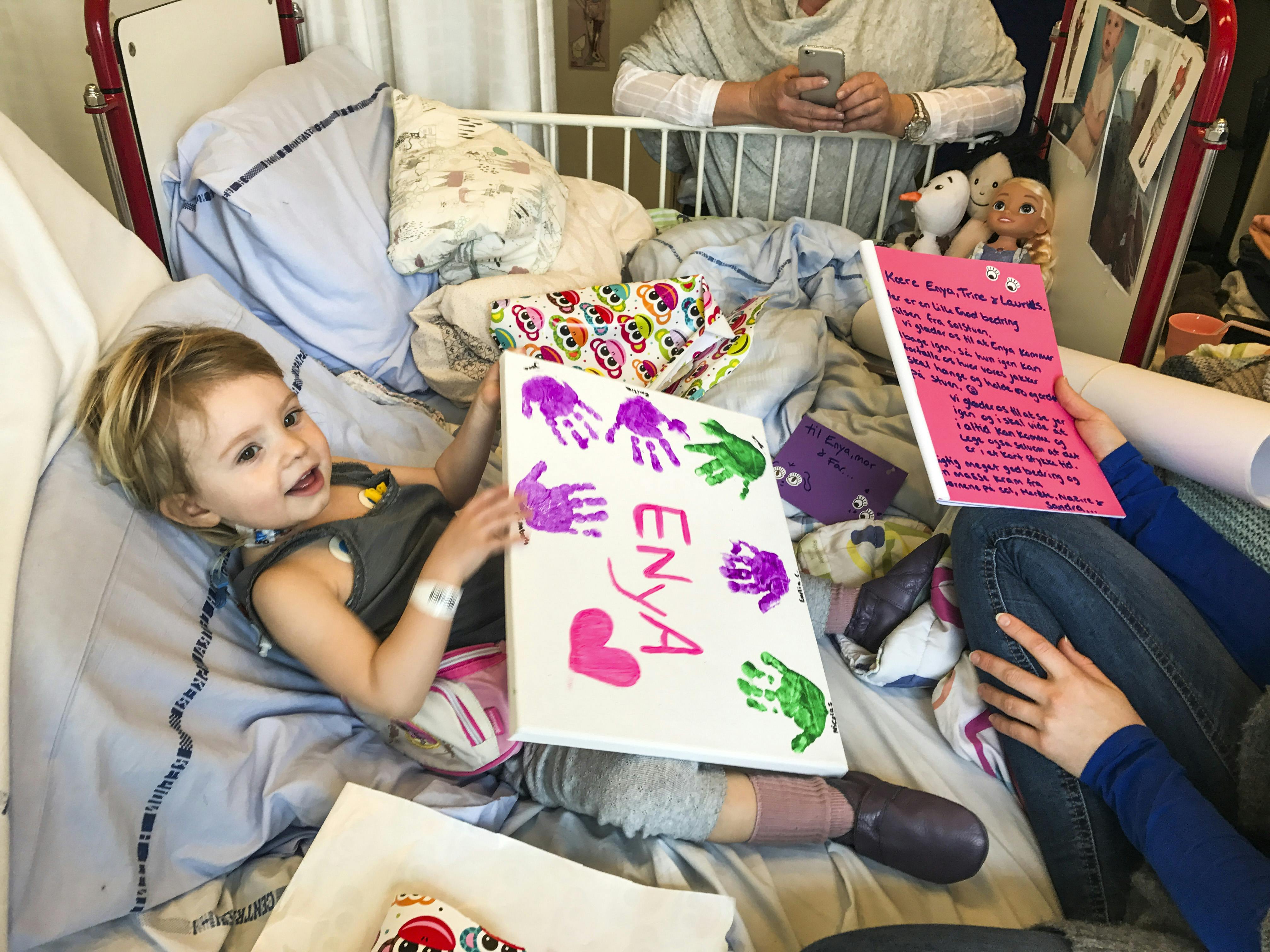 To-årigt barn ligger i hospitalsseng med en tegning, hun har fået i gave