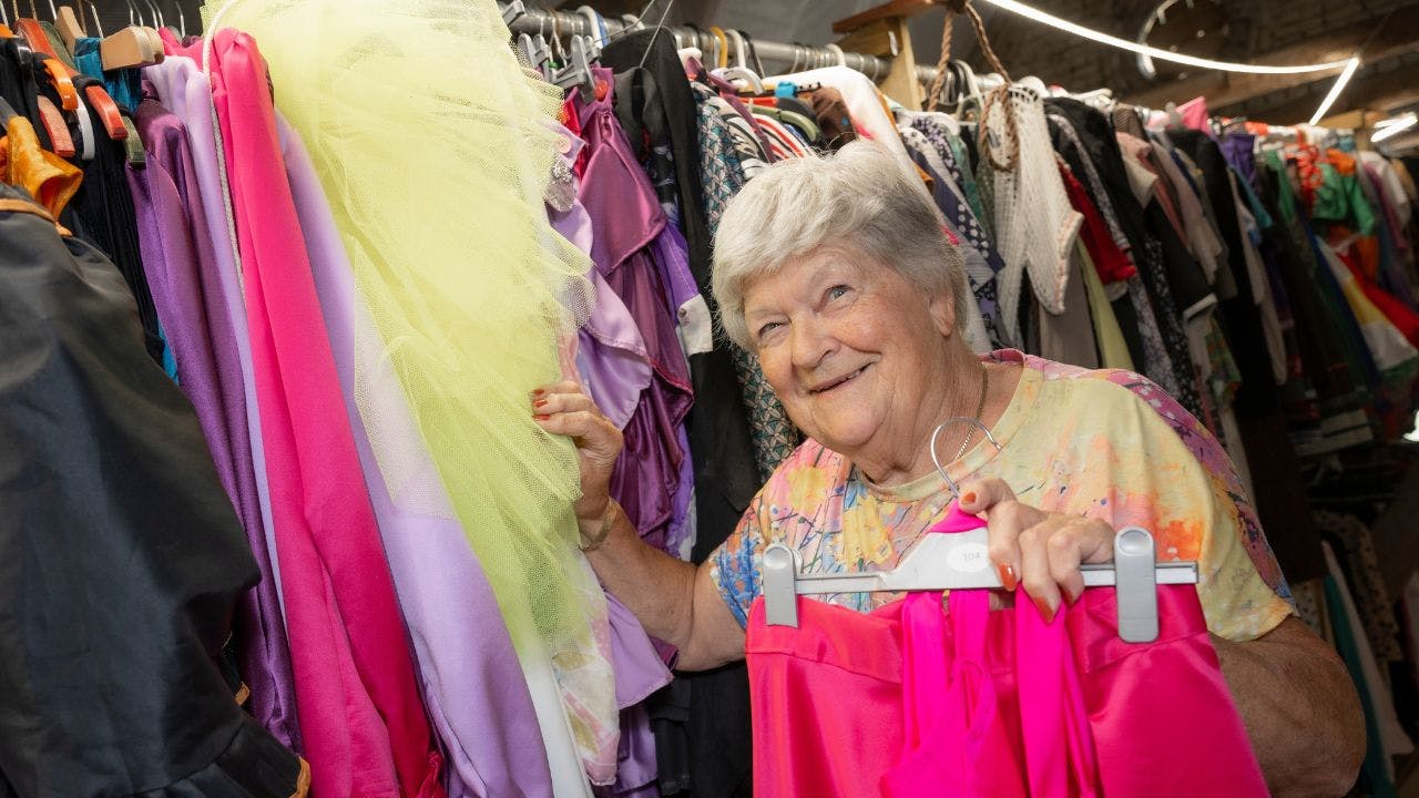 Ældre kvinde, der står blandt farverige kostumer