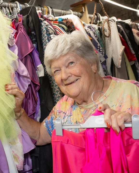 Ældre kvinde, der står blandt farverige kostumer