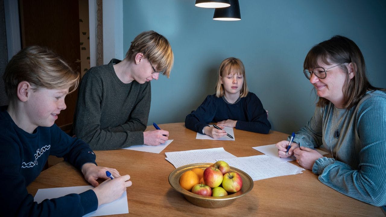 En kvinde og tre børn sidder ved et bord og skriver på papir