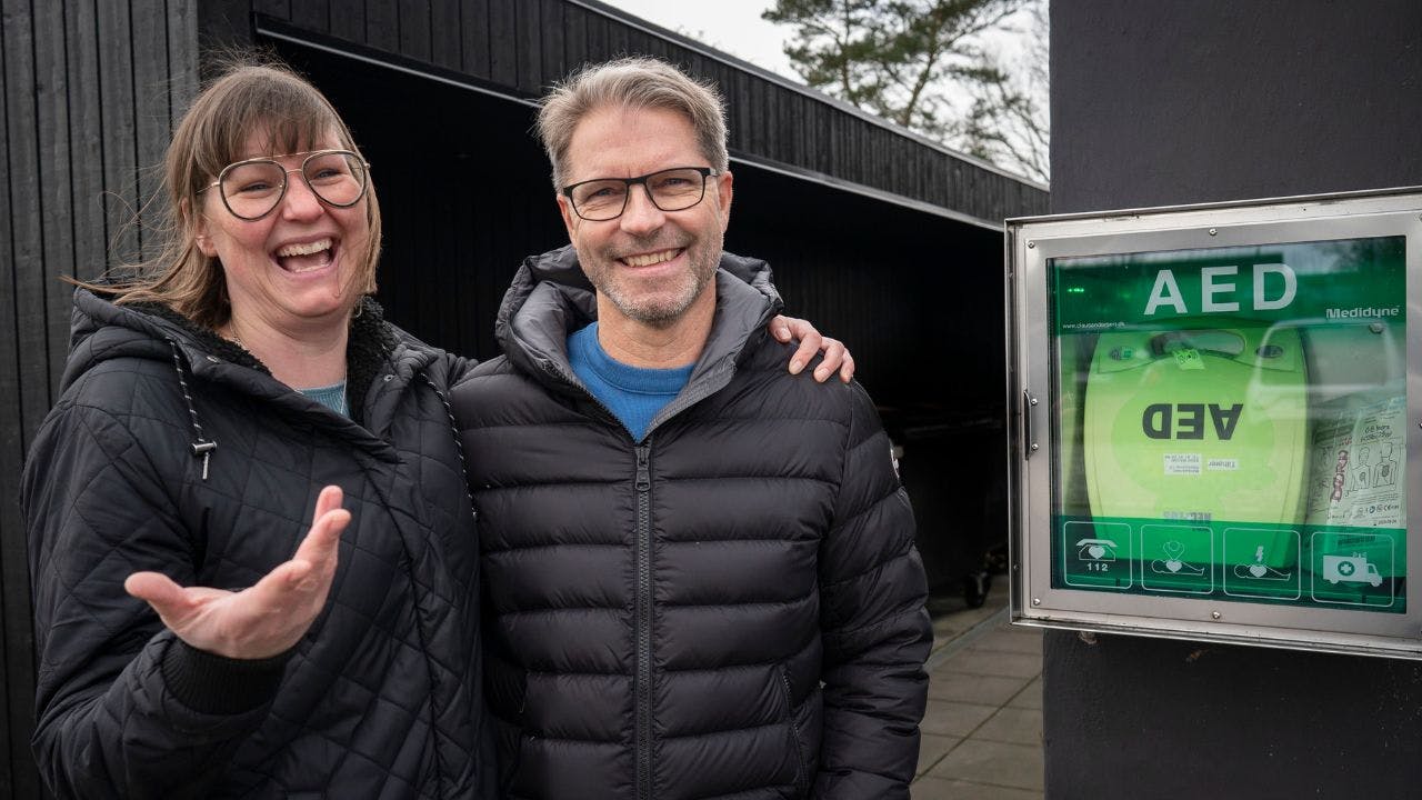 En dame og kvinde står smilende ved siden af en hjertestarter