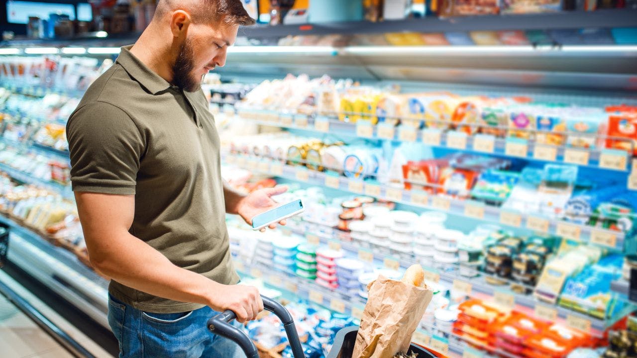 Mand står i supermarked med telefon i hånden