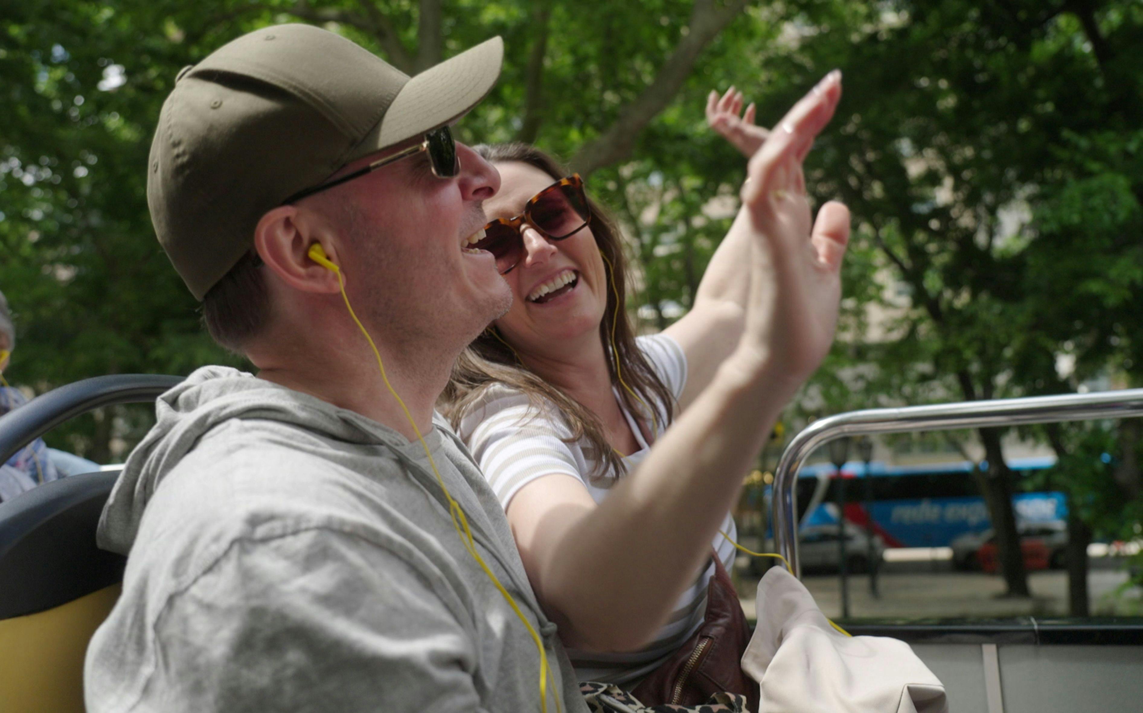 Et par, der sidder i en sightseeingbus og griner og peger.