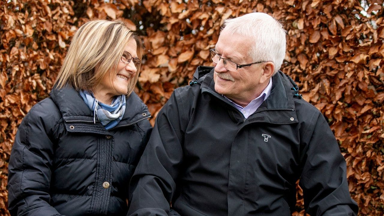 Et ældre ægtepar kigger smilende på hinanden på en bænk