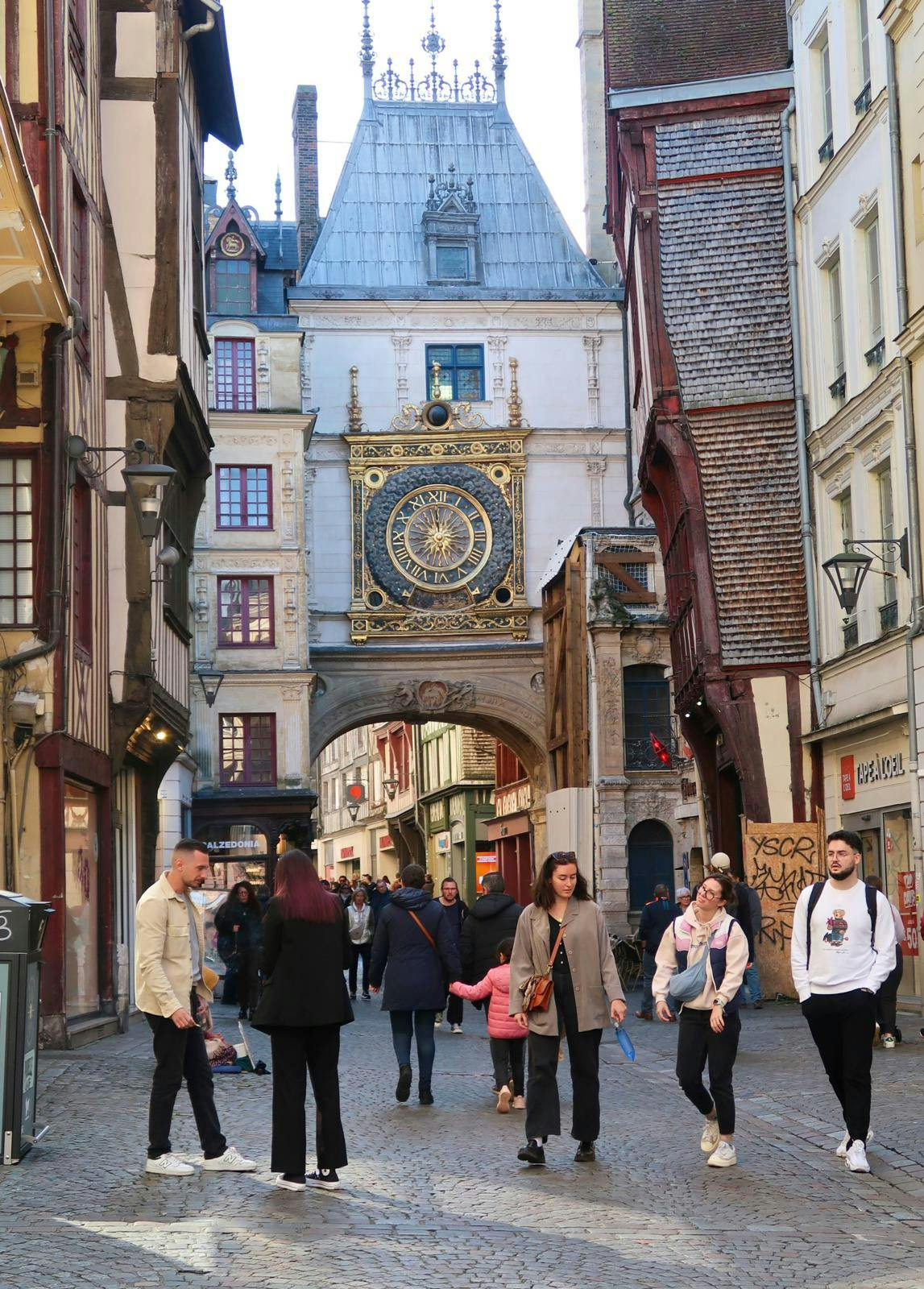 En gade med mennesker, der går under en port med et stort ur over.