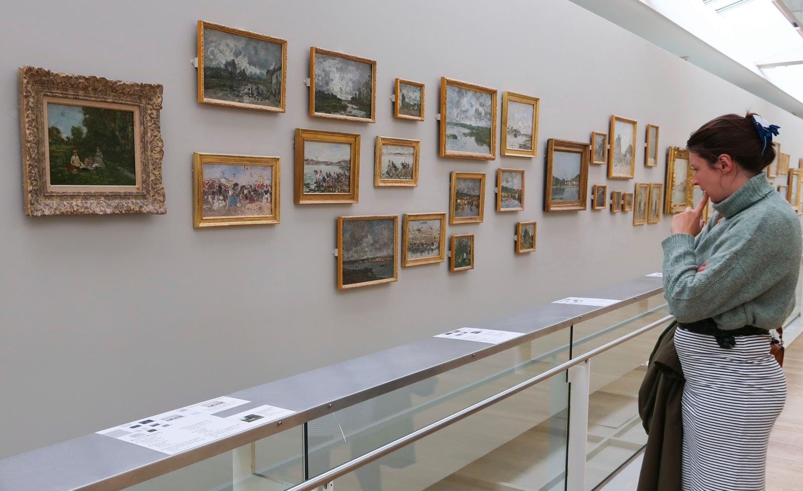 En kvinde, der står på et museum og kigger på malerier i små rammer.