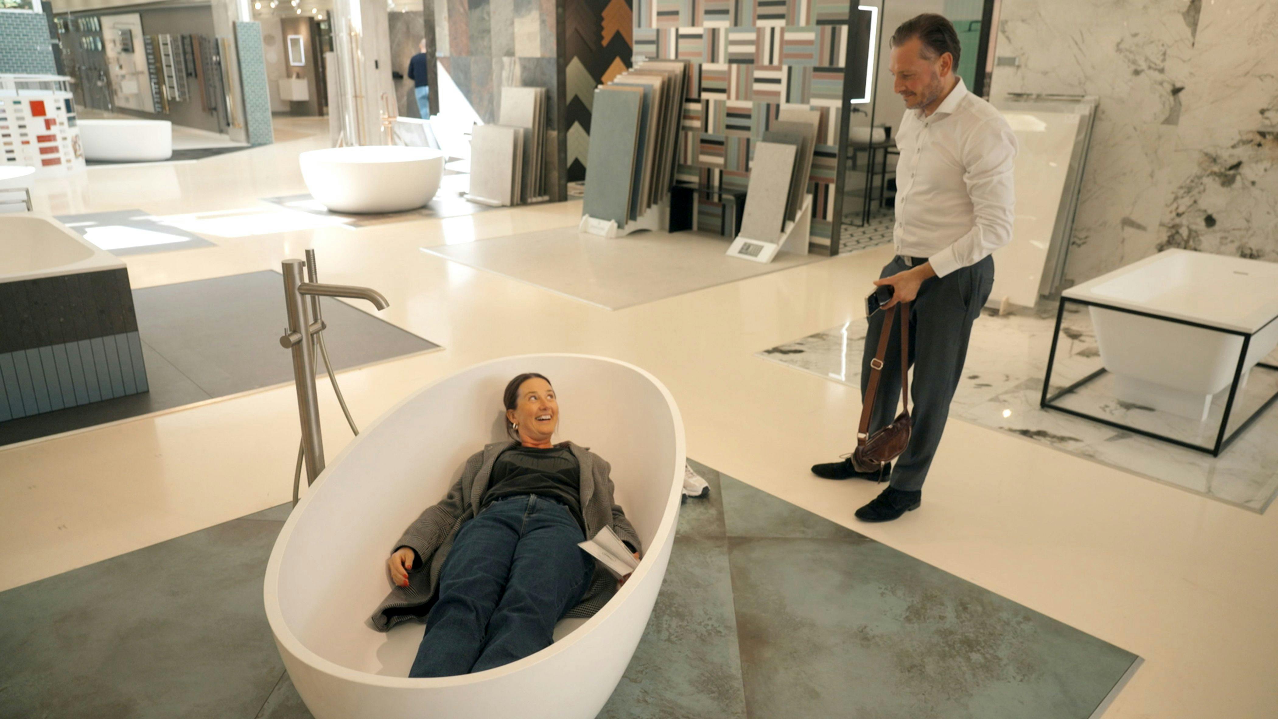 En mand, der står i et byggemarked og kigger på en kvinde i et badekar.